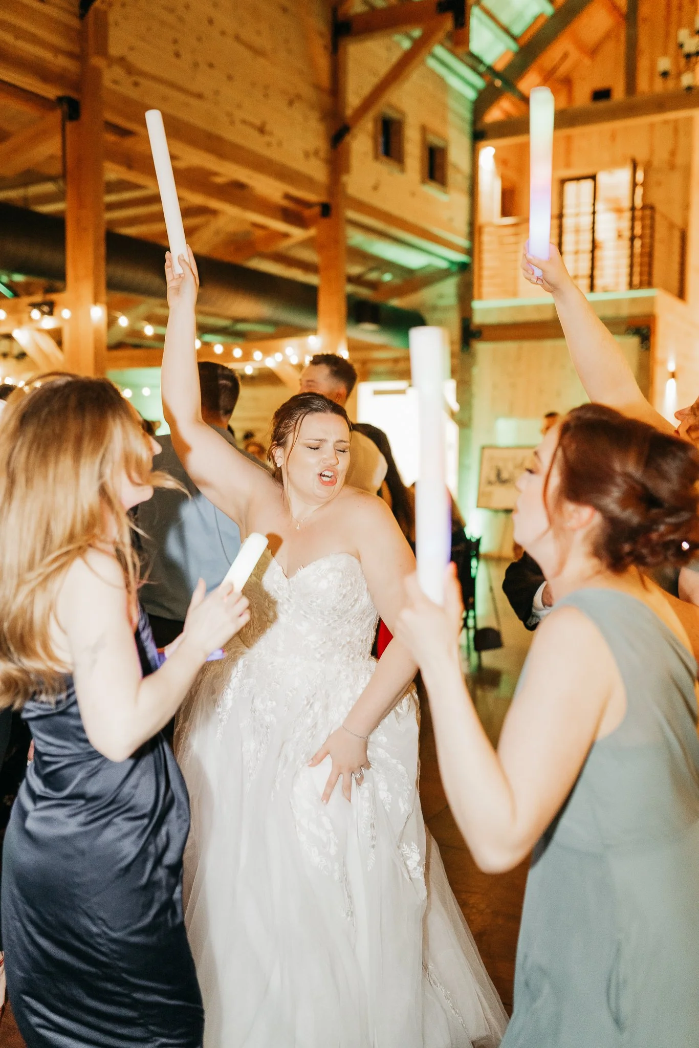 Bride dancing with friends during a wedding celebration, holding light-up sticks.