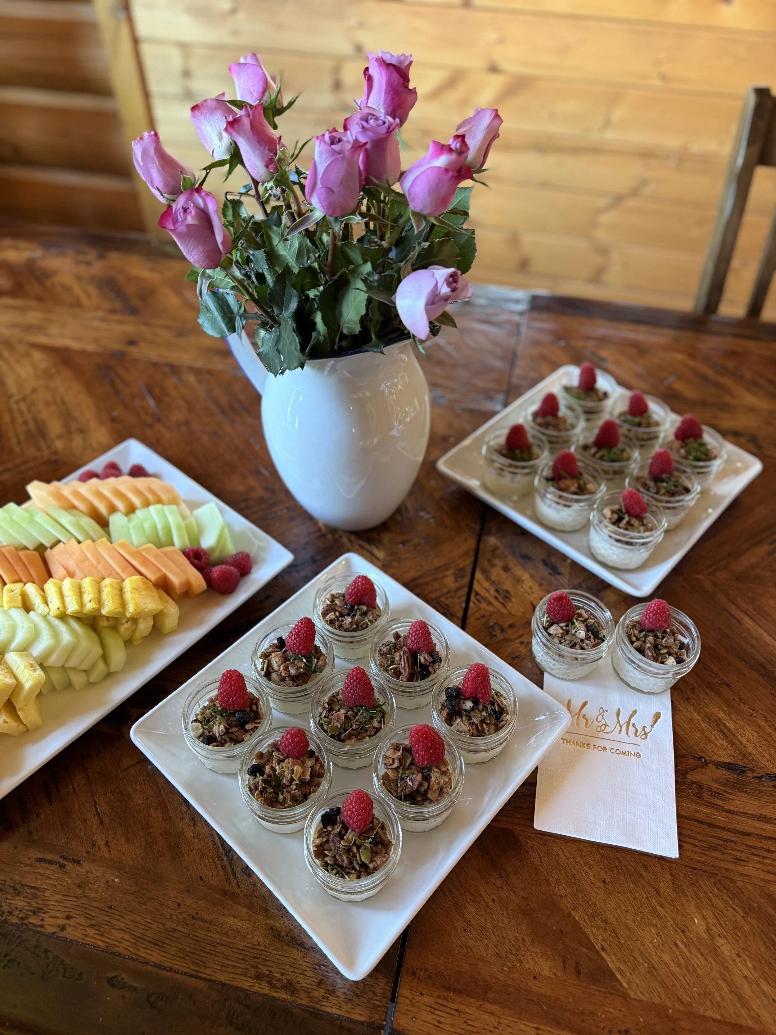 A Wedding Brunch with a fruit platter with melon, cantaloupe and pineapple slices. Mini yogurt parfaits with granola and topped with raspberries.