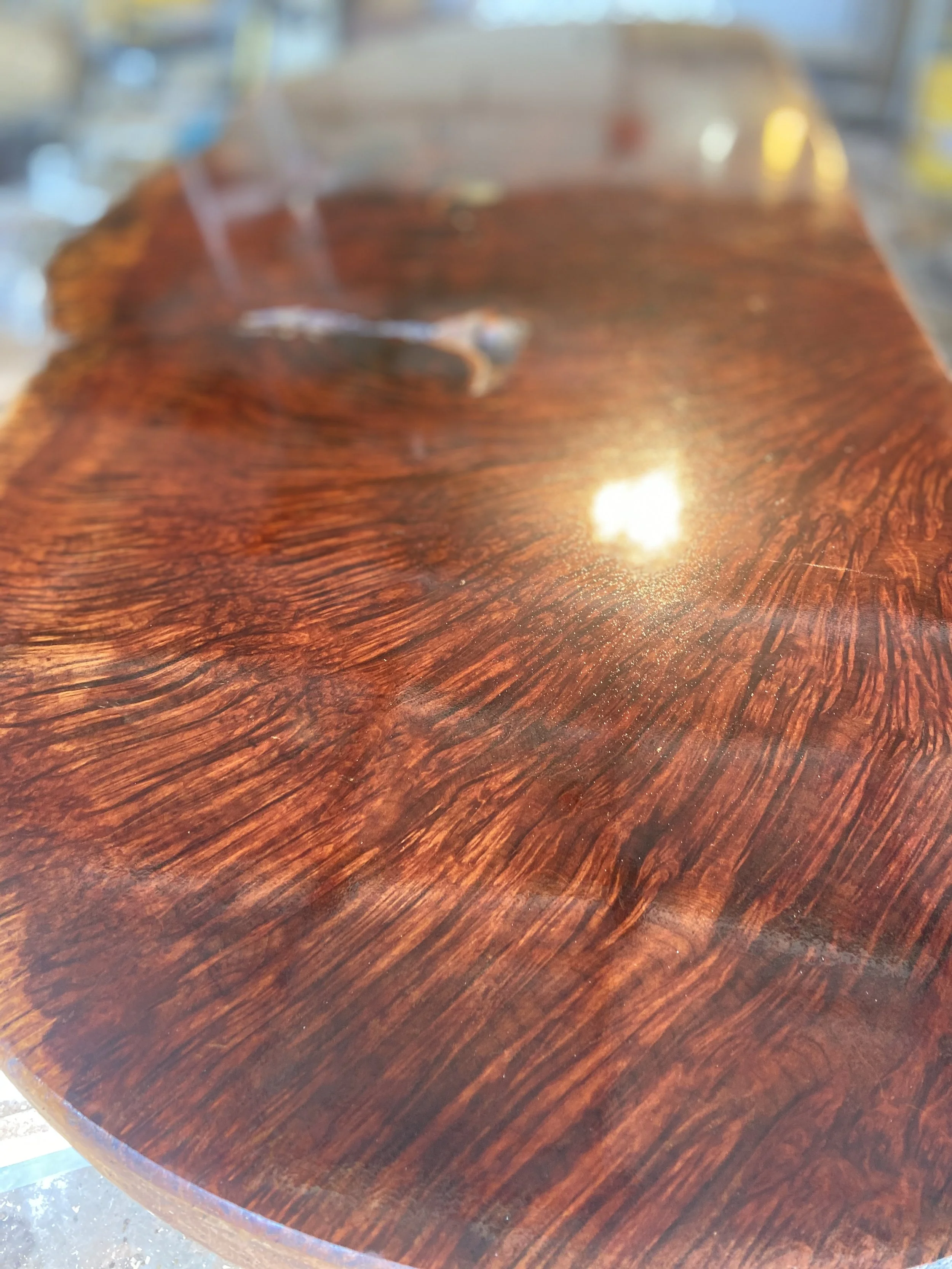 Close-up of a polished wooden surface with a rich, dark reddish-brown color and visible wood grain patterns.