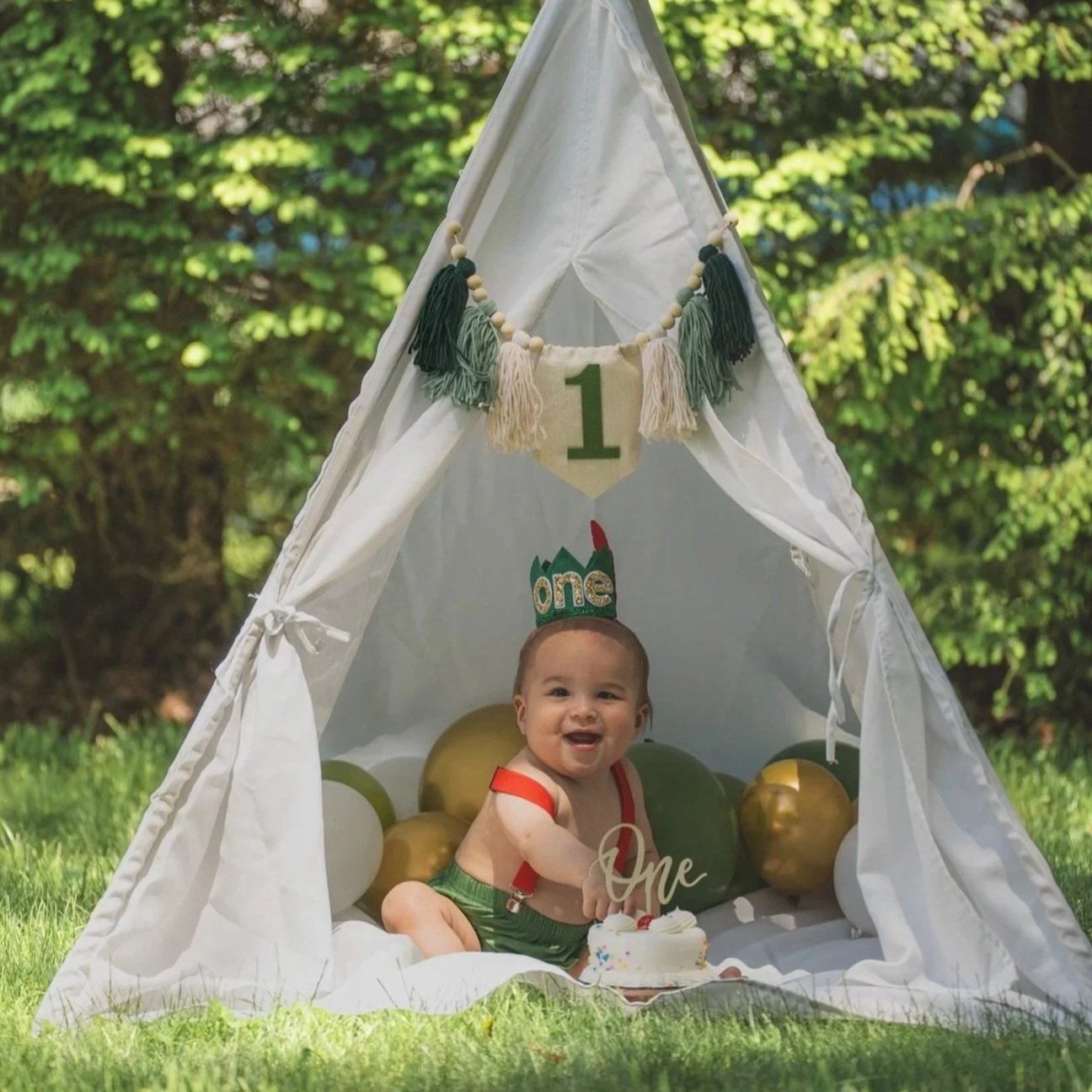 one year old baby boy in inside a tent on a yard smashing hands into birthday cake