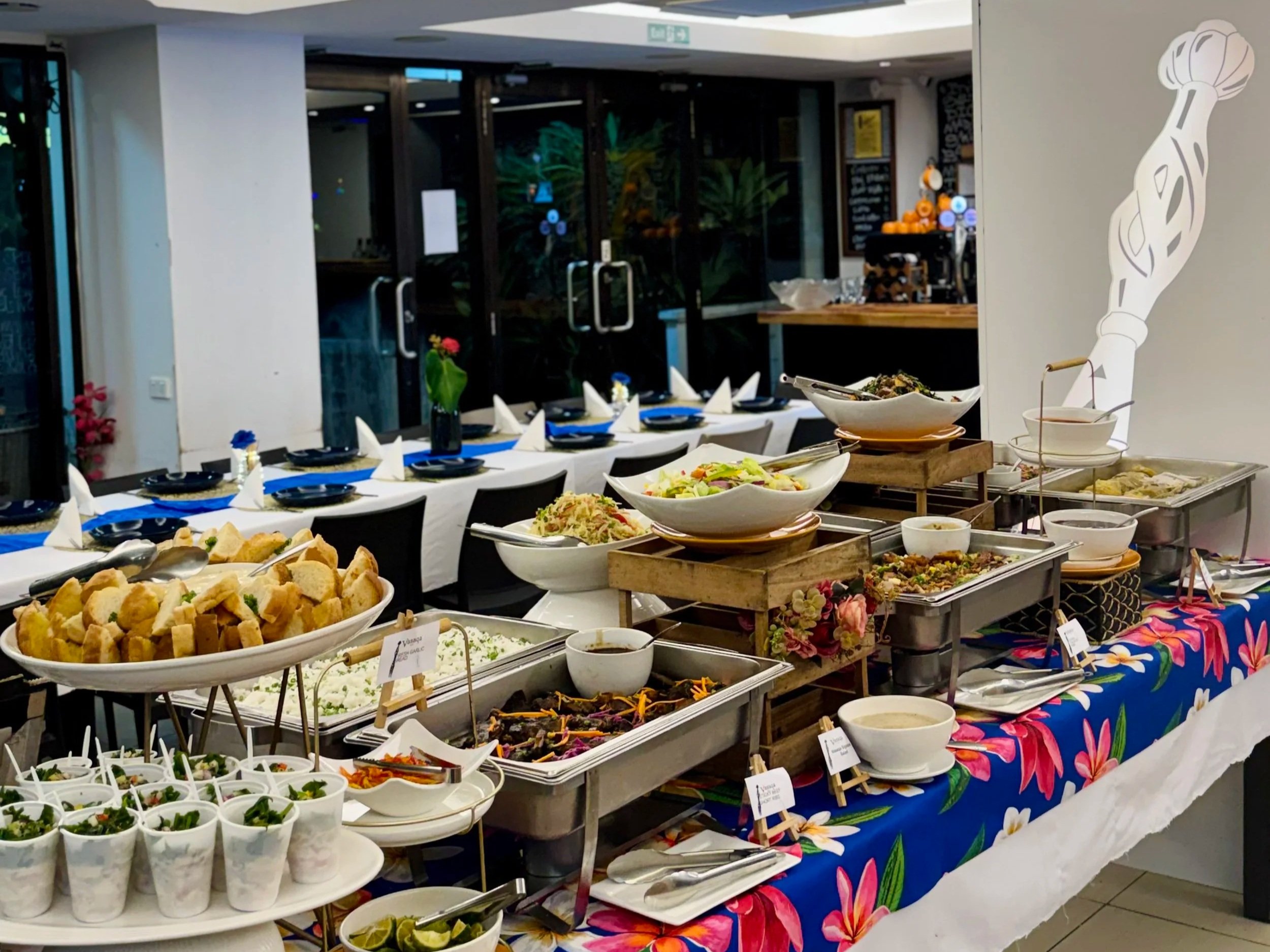 Buffet table with various dishes, salads, and appetizers in a restaurant in fji or event setting, with a floral tablecloth and decorative elements.