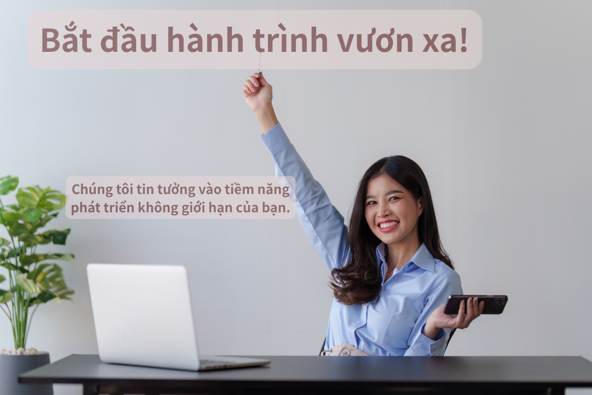 A young woman with dark hair and a blue shirt sitting at a desk, smiling and raising her fist, holding a smartphone in her other hand. There is a laptop and a potted plant on the desk, and Vietnamese text overlays the image.