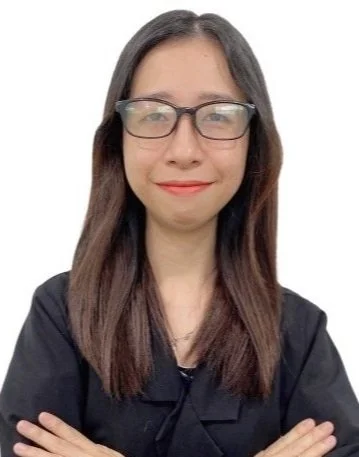 A woman with long hair and glasses wearing a black top, smiling with her arms crossed.