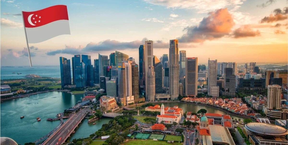 Aerial view of Singapore skyline with Singapore flag, featuring skyscrapers, Marina Bay, and a mix of modern and historic architecture at sunset.