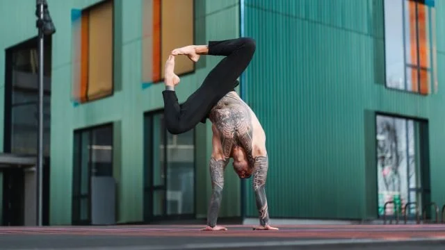 Man performing a handstand on a rooftop with colorful building windows in the background.
