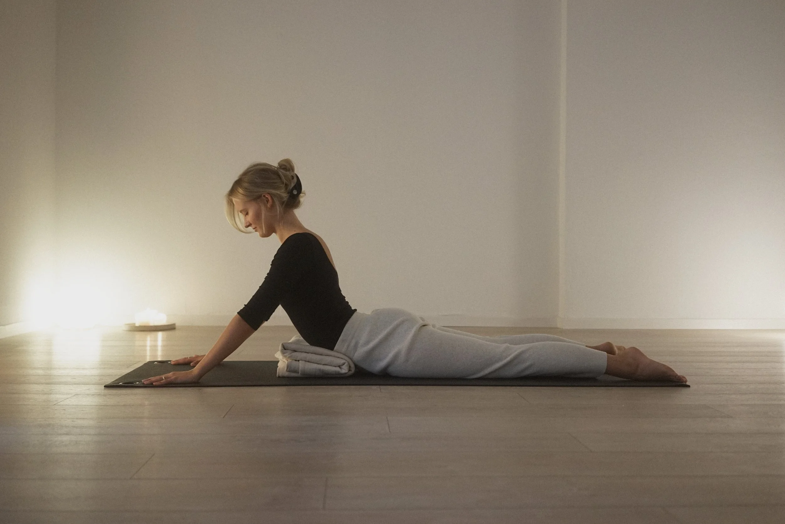 A woman practicing yoga in a minimalist room, positioned in a Low Cobra pose with her palms on the ground and her chest lifted.