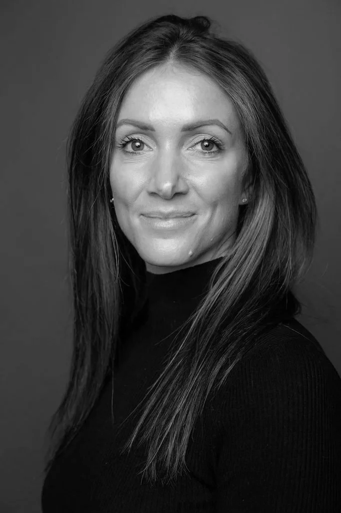 Black and white portrait of a woman with long, straight hair, smiling slightly, wearing a dark turtleneck, against a plain background.