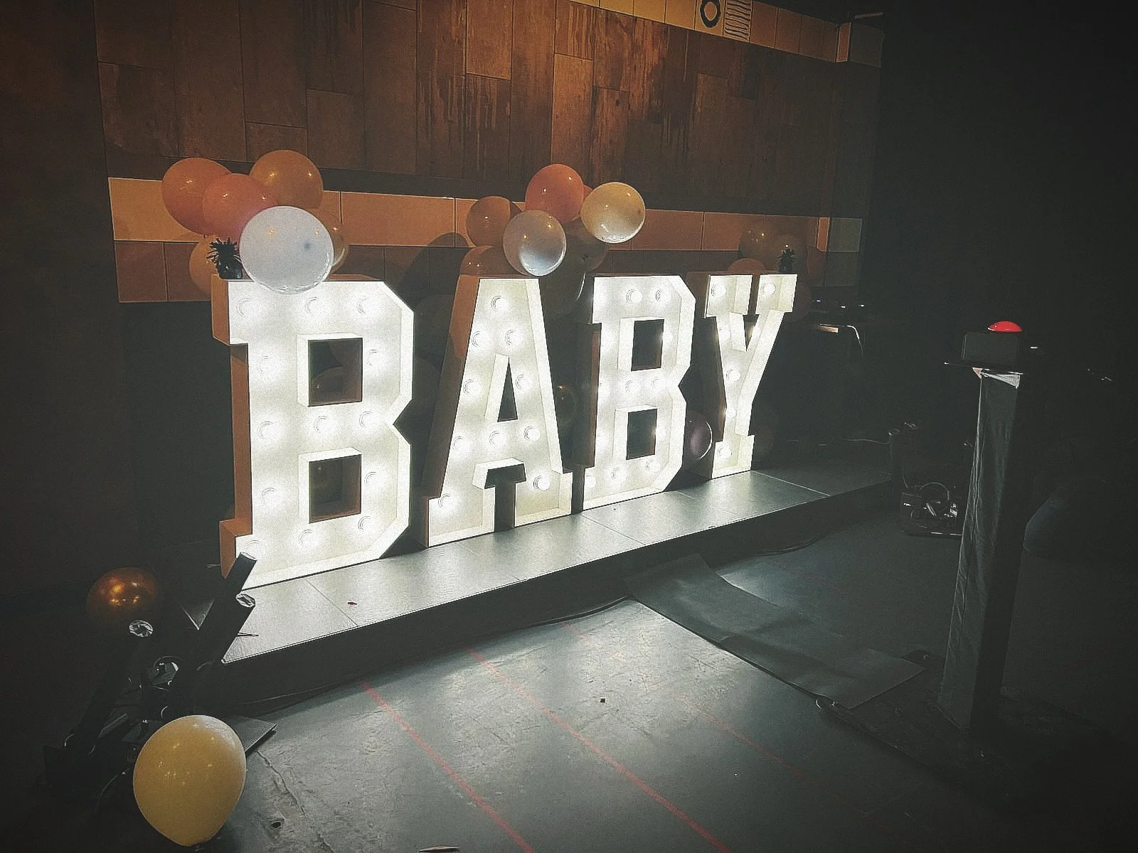 Verlichte letters die het woord 'BABY' vormen, omringd door ballonnen en geplaatst op een podium.