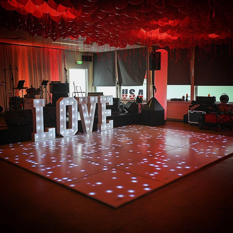Dansvloer met verlichte "LOVE"-letters en muziekpodium op achtergrond.