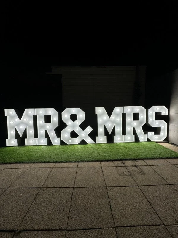 Verlichte letters 'MR & MRS' op een grasveld in de nacht.