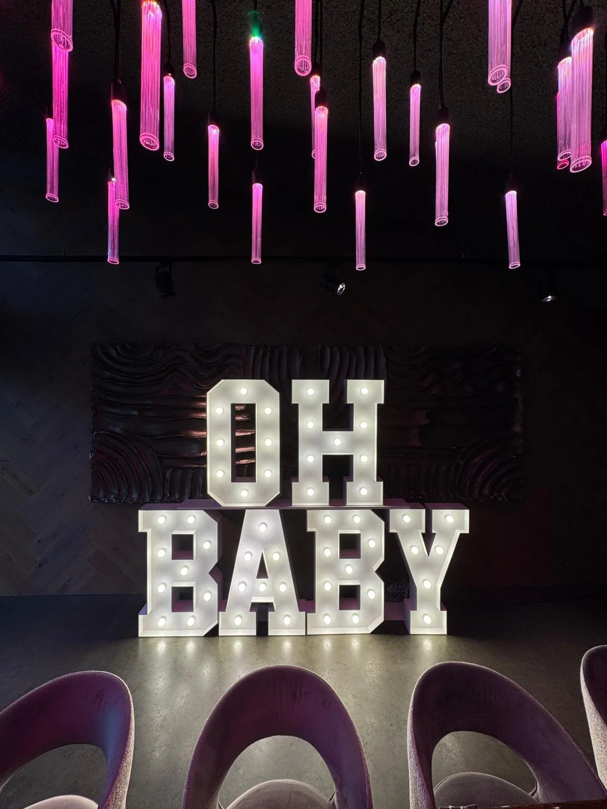 Verlichte letters met "OH BABY" omgeven door blauwe en witte ballonnen.