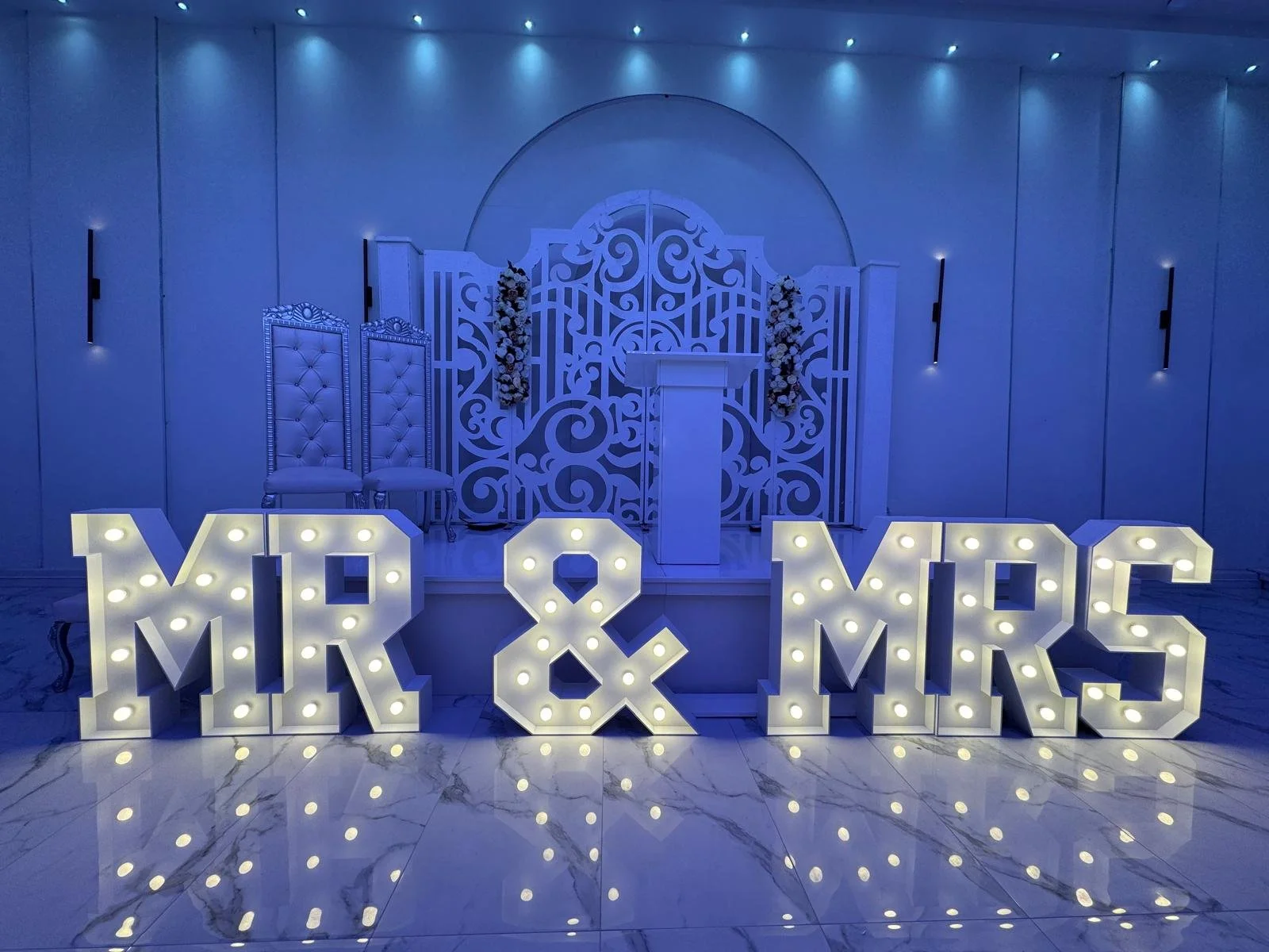 Verlichte letters "MR & MRS" op gras en tegels in de avond.
