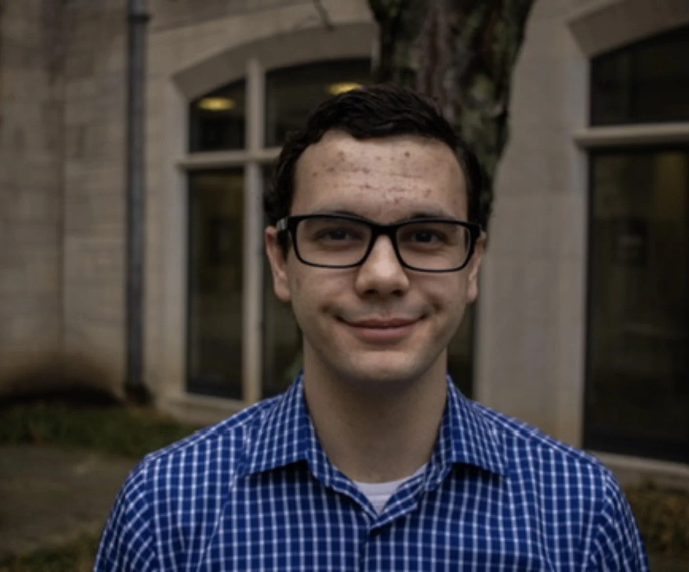 Photo of Izzy Frieze, a white woman, wearing a black and white checkered summer dress topped with a crimson graduation stole