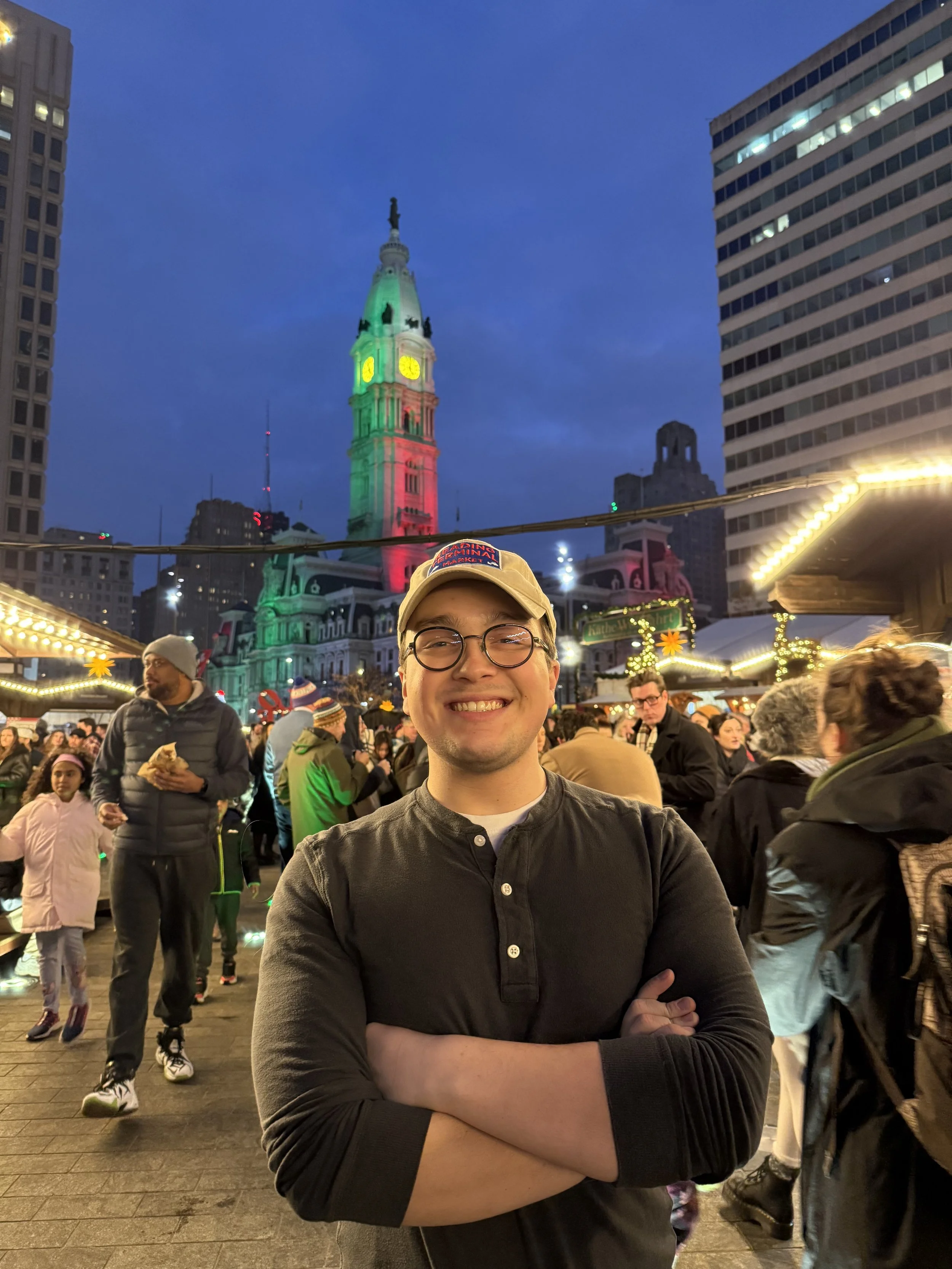 Picture of Kye Benford, a Black man with glasses, wearing a light blue dress shirt with a black suit jacket, sitting on a staircase