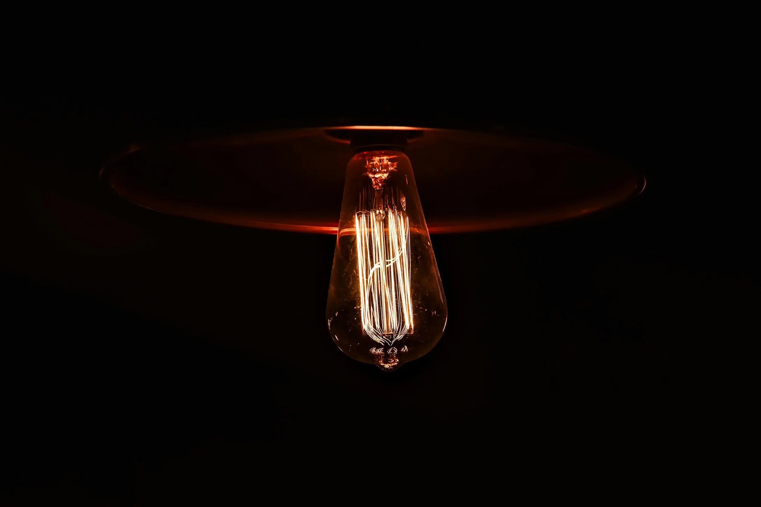Close-up of an illuminated Edison-style filament light bulb against a dark background.