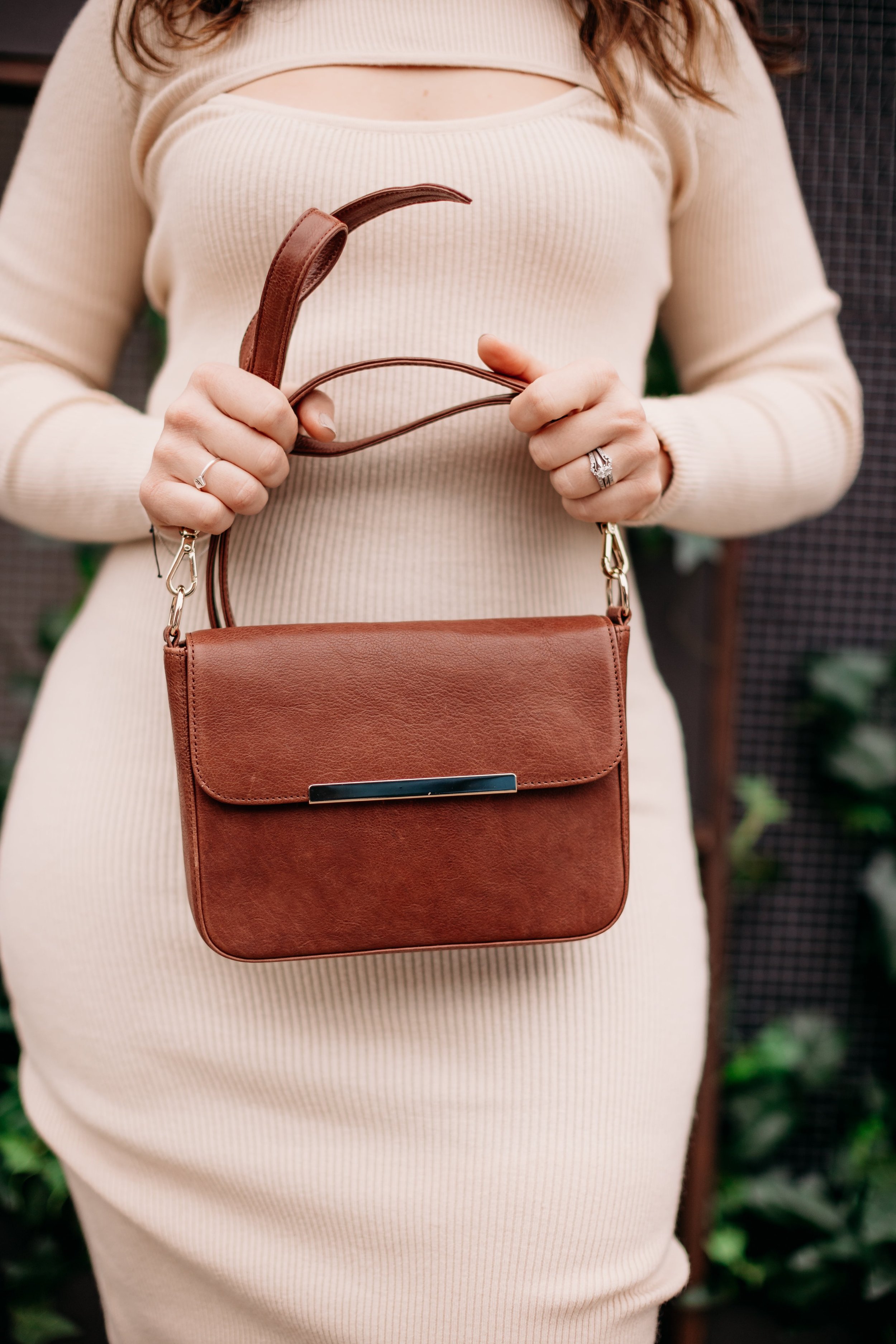 Woman holding a brown leather handbag, wearing a beige ribbed sweater dress.