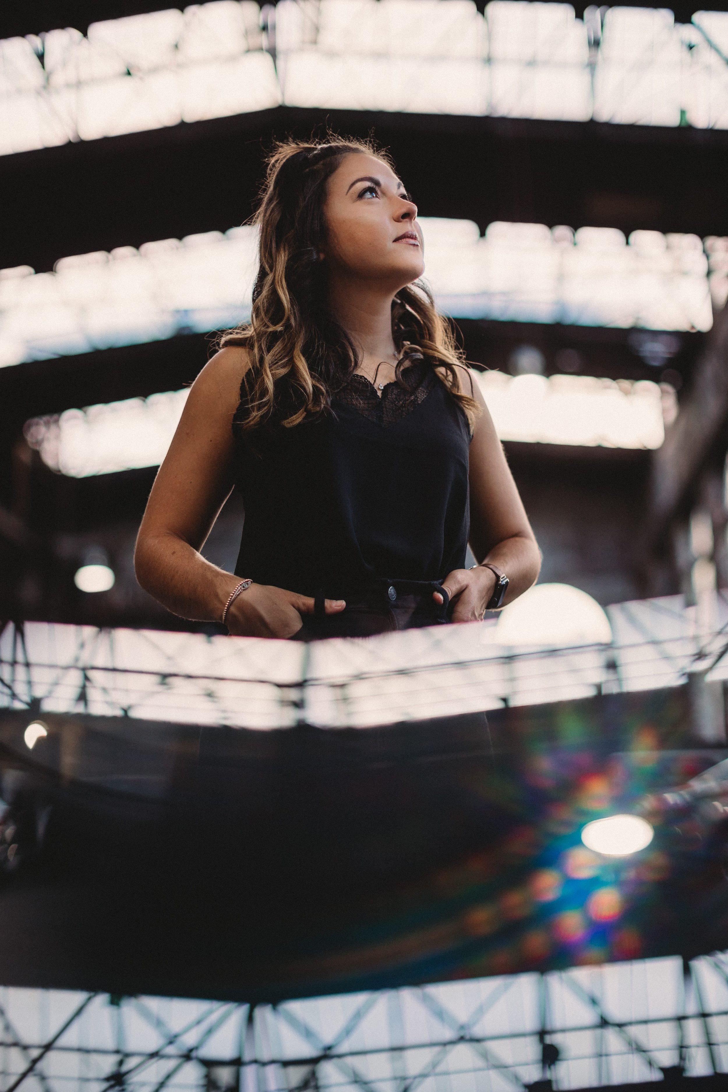 Woman in black top inside an industrial building, looking upwards with a reflective, prismatic effect in the foreground.