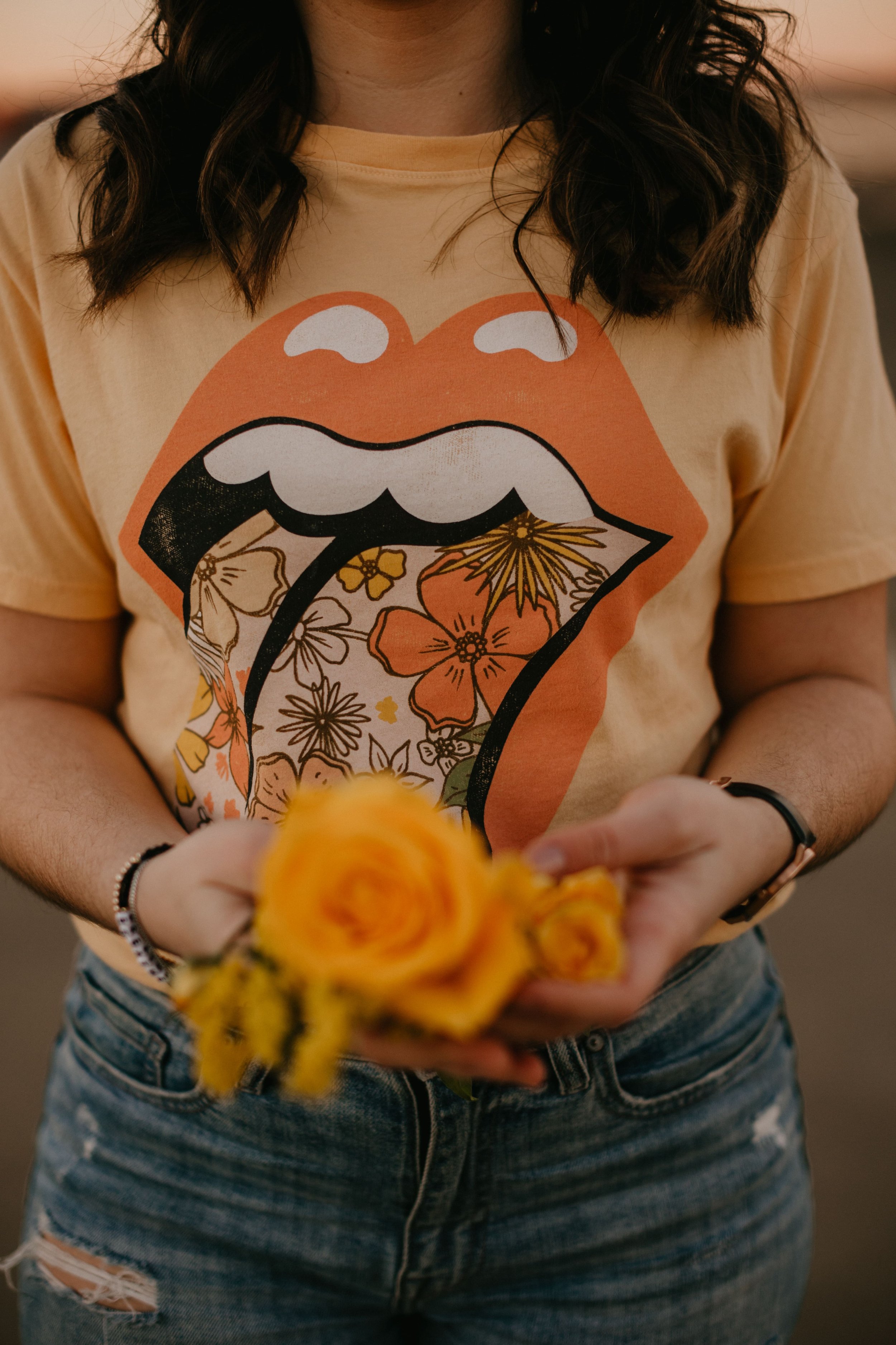 Person wearing a t-shirt with a floral tongue design, holding yellow roses in hands.