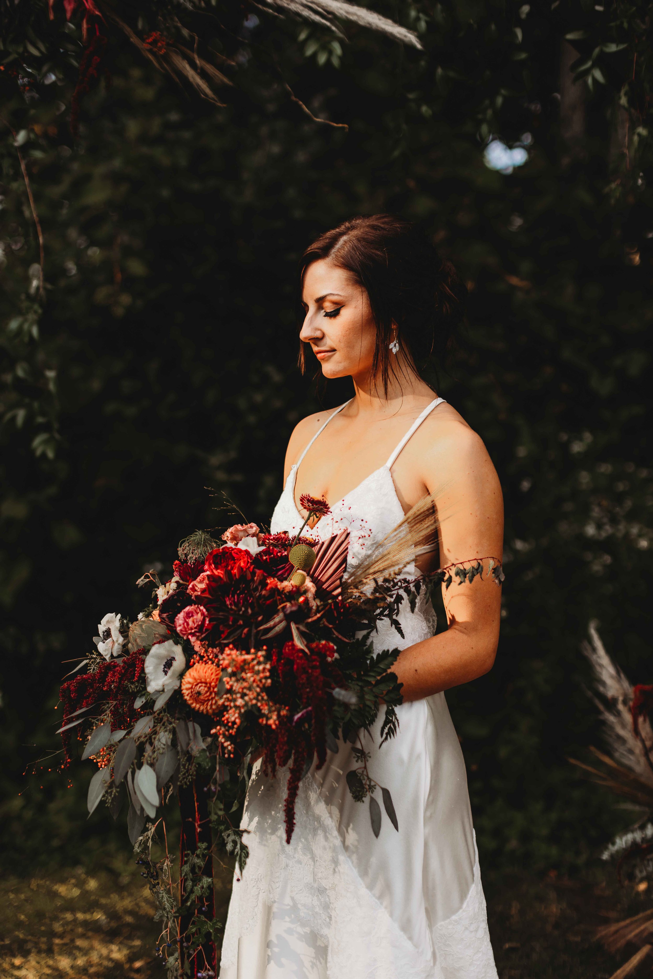 Bride holding vibrant bouquet with red and orange flowers, wearing a white dress, in outdoor setting.