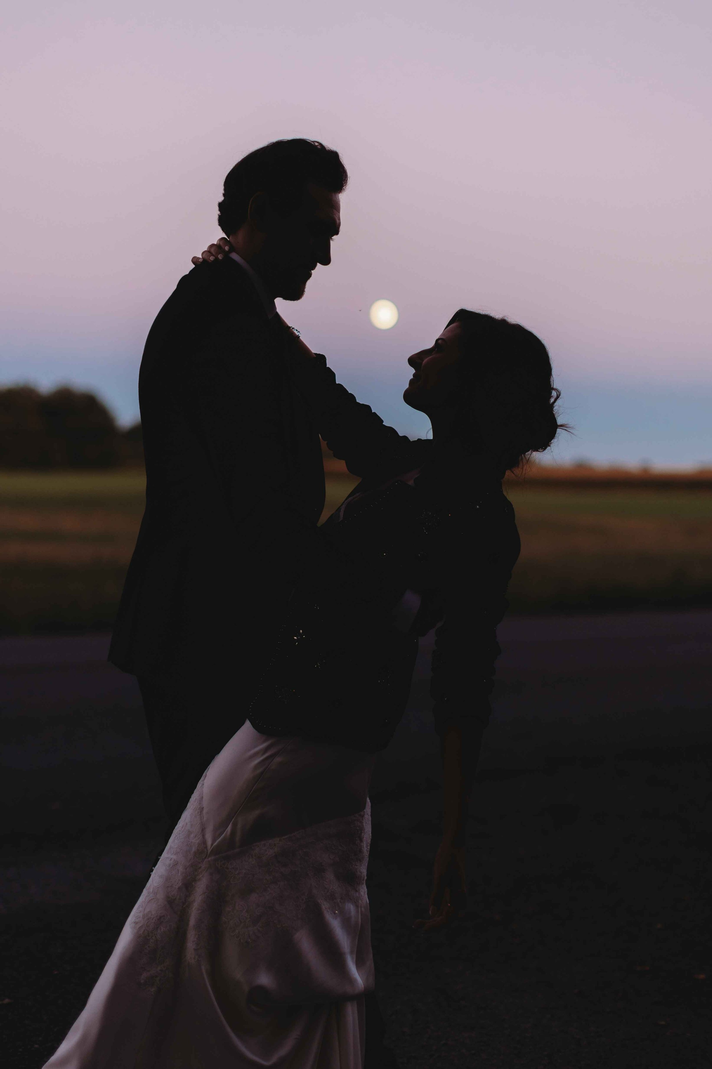 Silhouette of a couple dancing at sunset with the moon in the background.