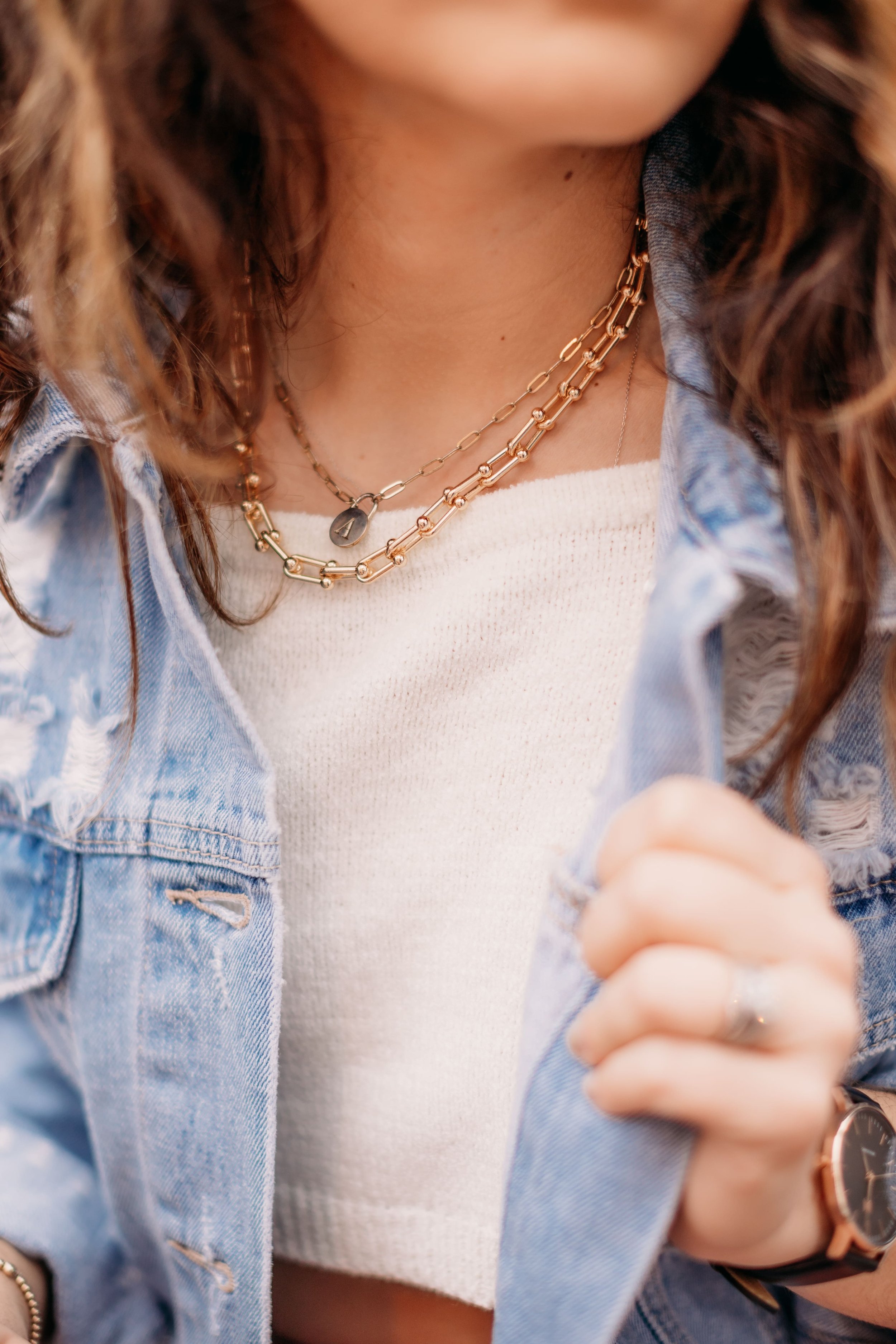 Close-up of a woman wearing layered necklaces and a denim jacket over a white top.
