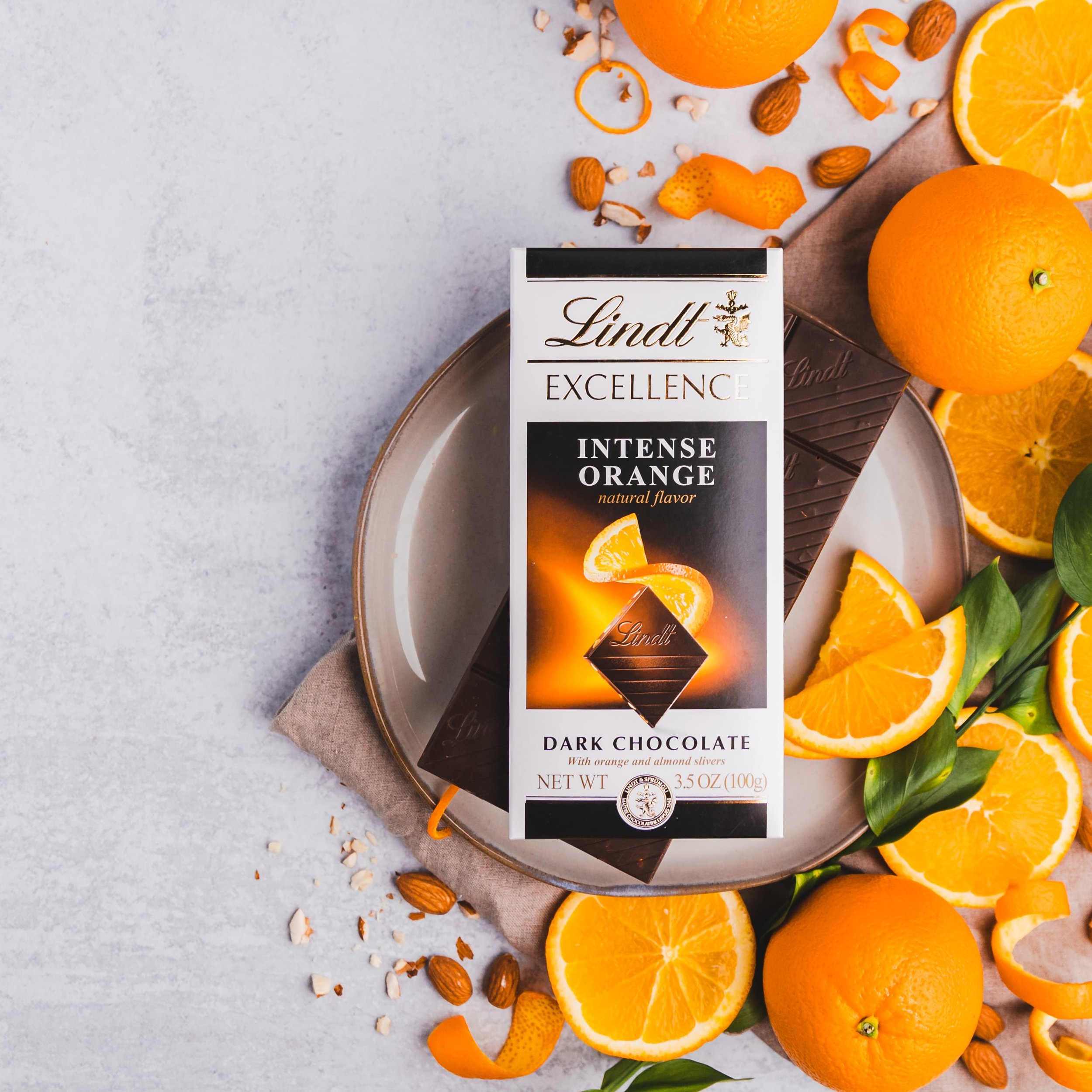 Lindt Excellence Intense Orange dark chocolate bar on a plate surrounded by orange slices, almonds, and zest.