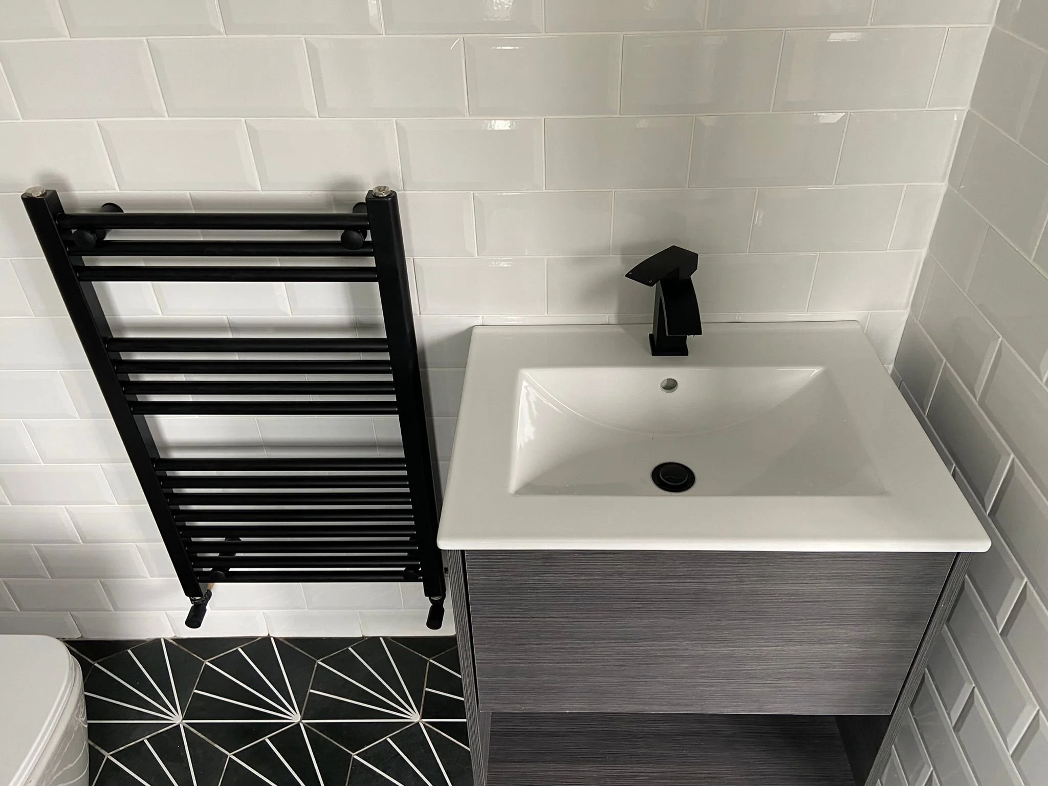 Black radiator on white tiled wall beside a beautiful grey sink cabinet with a white sink.