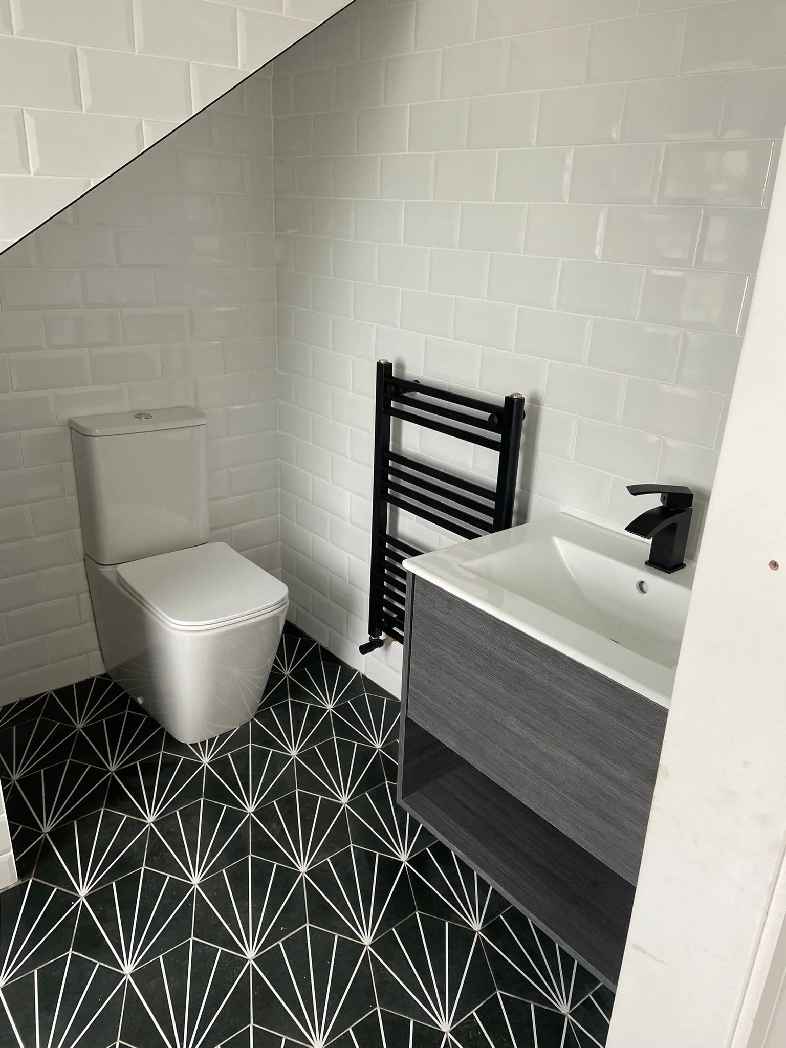 Bathroom in an attic with black and white patterned tiles, a white sink, a black wall mounted radiator and a grey sink cabinet.