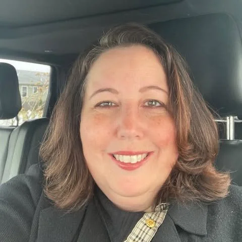 A woman with shoulder-length brown hair and light skin smiling inside a car.