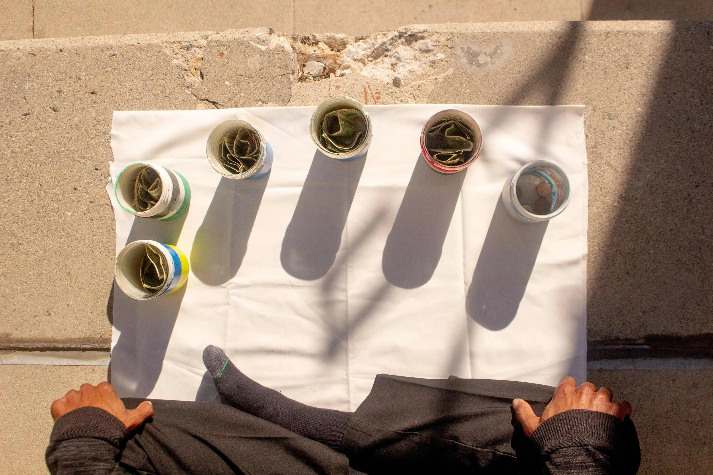 Overhead view of a person standing next to a table with five cups of coffee, each containing a napkin, casting long shadows on a white cloth.