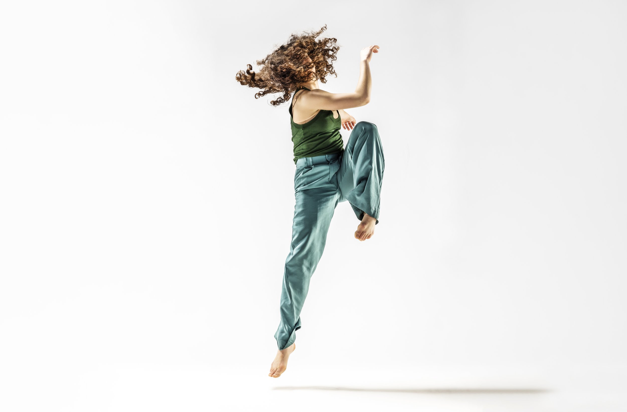 A woman with curly hair jumping mid-air against a plain white background.