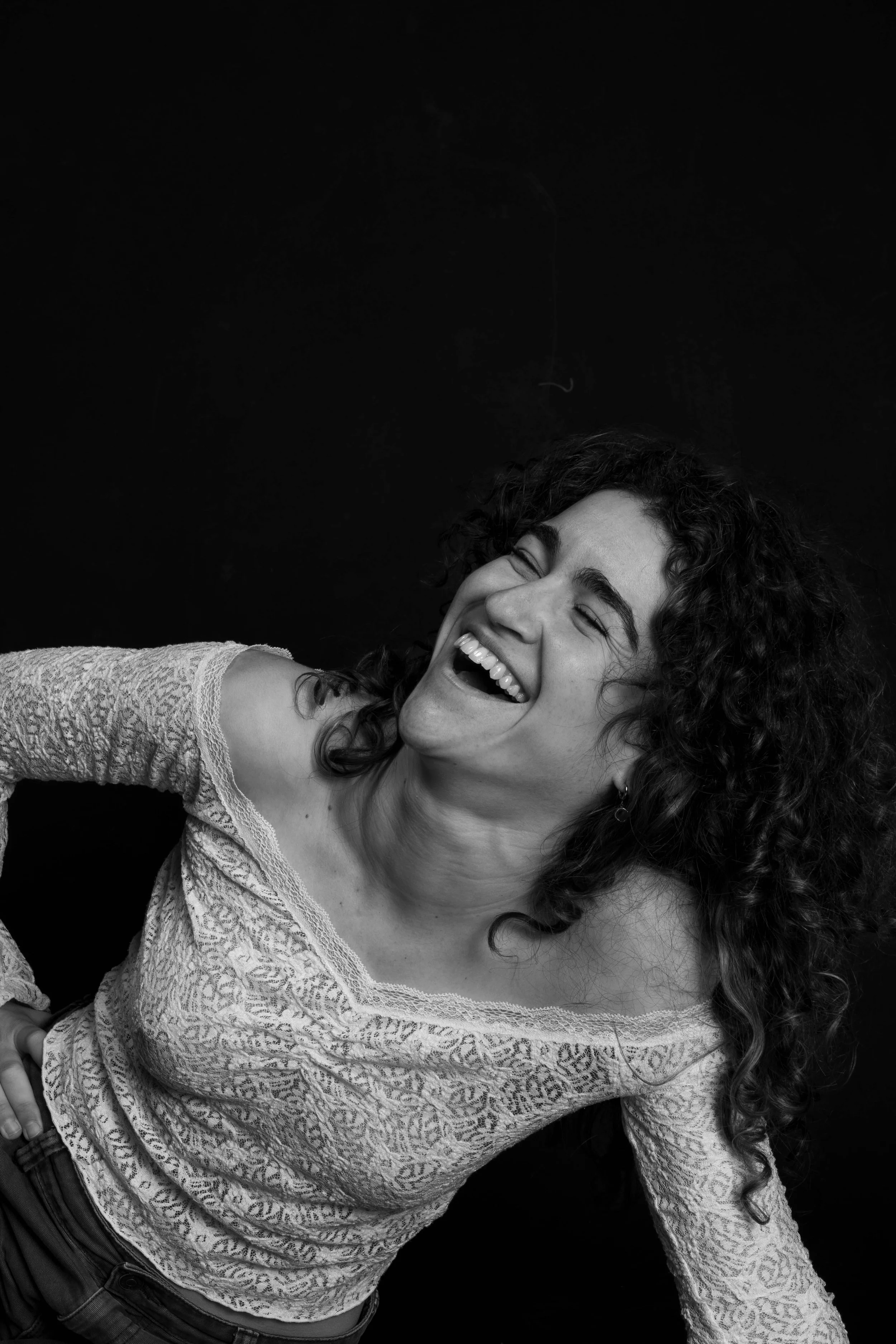 A woman laughing, head tilted back, in a black and white photo, wearing an off-shoulder lace top.