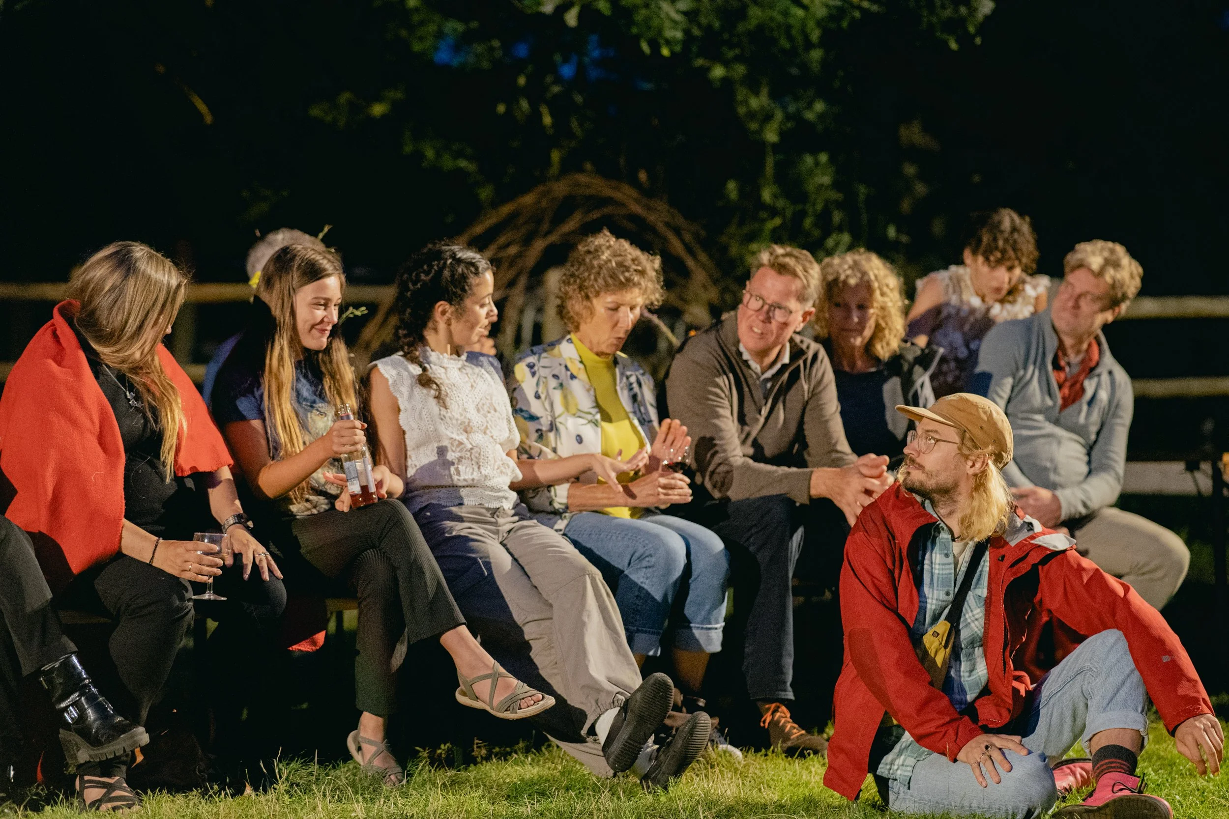 People sitting on benches in a park at night, having a casual conversation.
