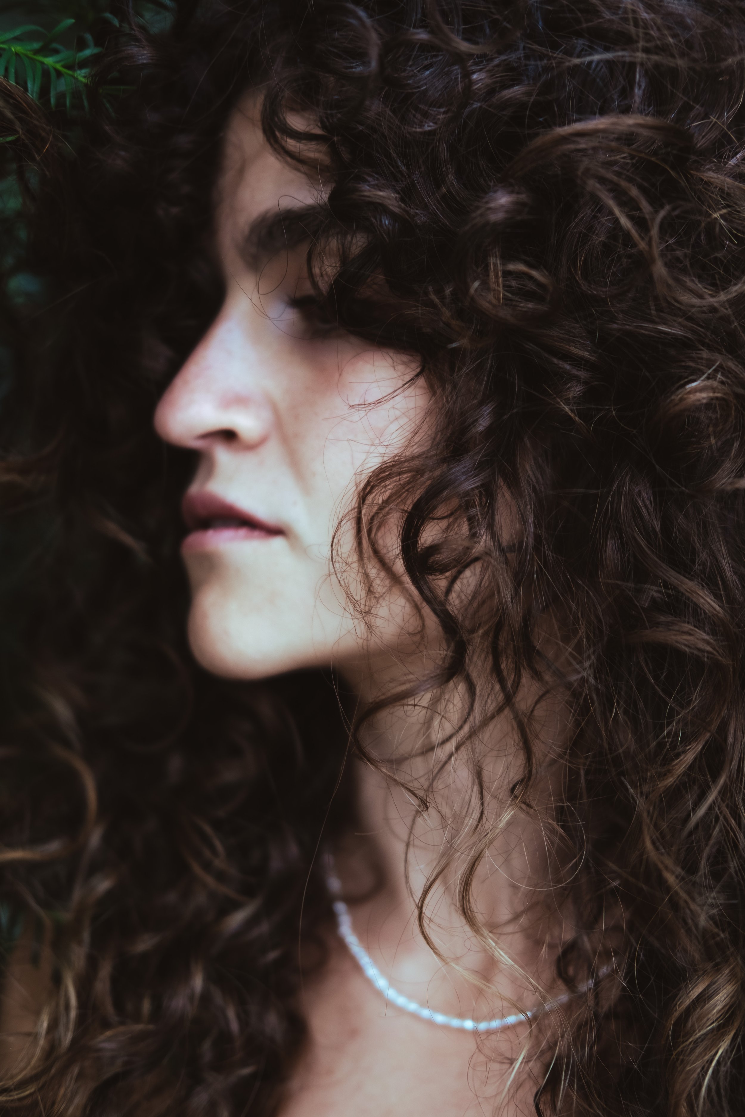 Close-up profile of a woman with dark curly hair and a pearl necklace.