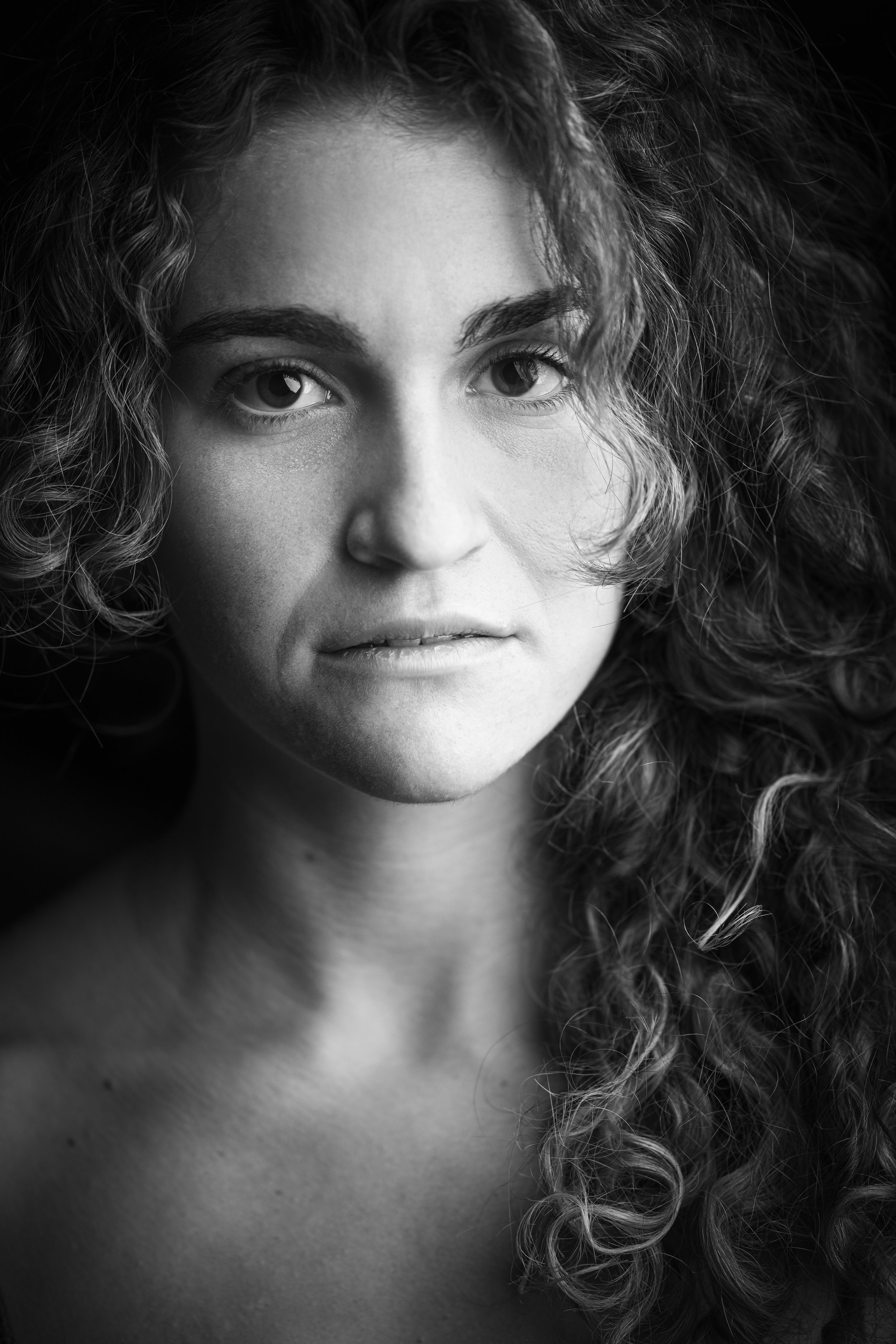 Close-up black and white portrait of a woman with curly hair, looking directly at the camera.