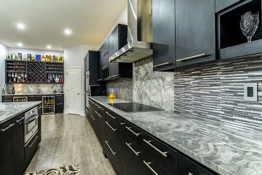 Modern kitchen with black cabinets, gray marble countertops, a wine rack, a wine cooler, and a glass cabinet.