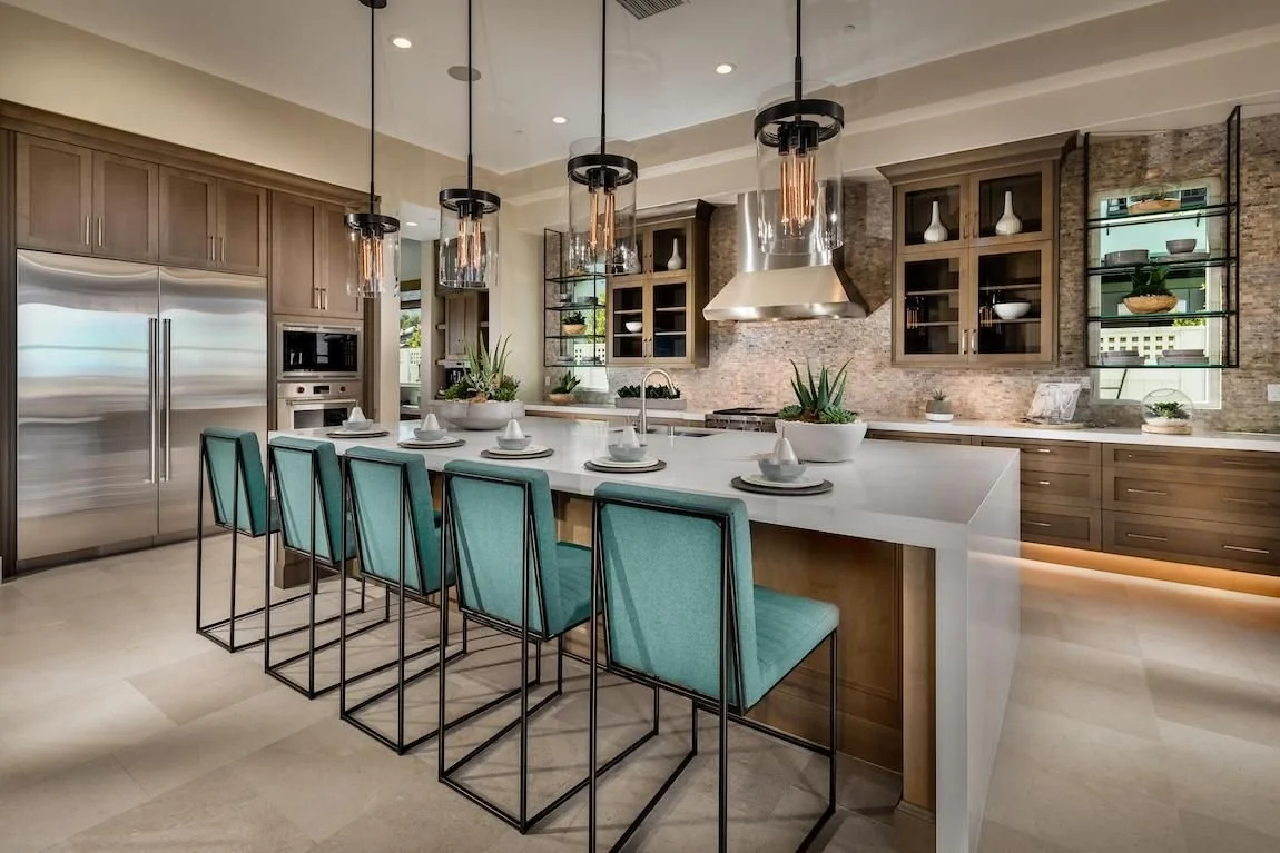 Modern kitchen with a large white island counter and turquoise bar stools, stainless steel appliances, open shelving, and a textured brick wall.