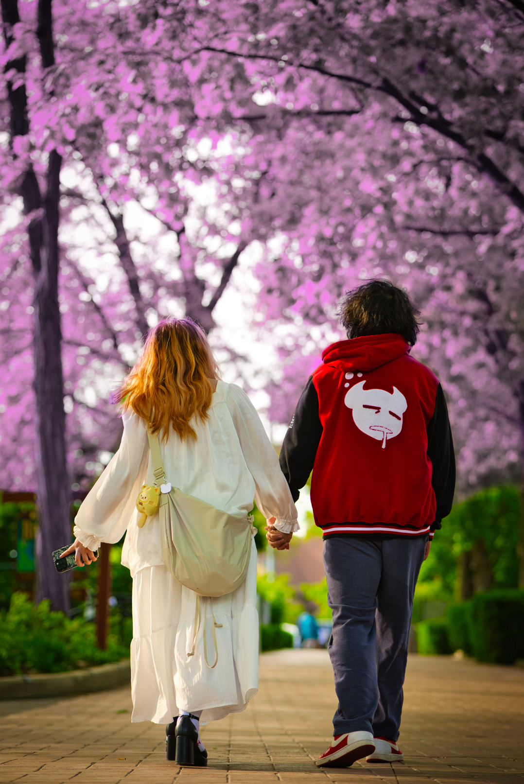 A couple walking hand in hand on a path lined with cherry blossom trees in full bloom, during daytime.
