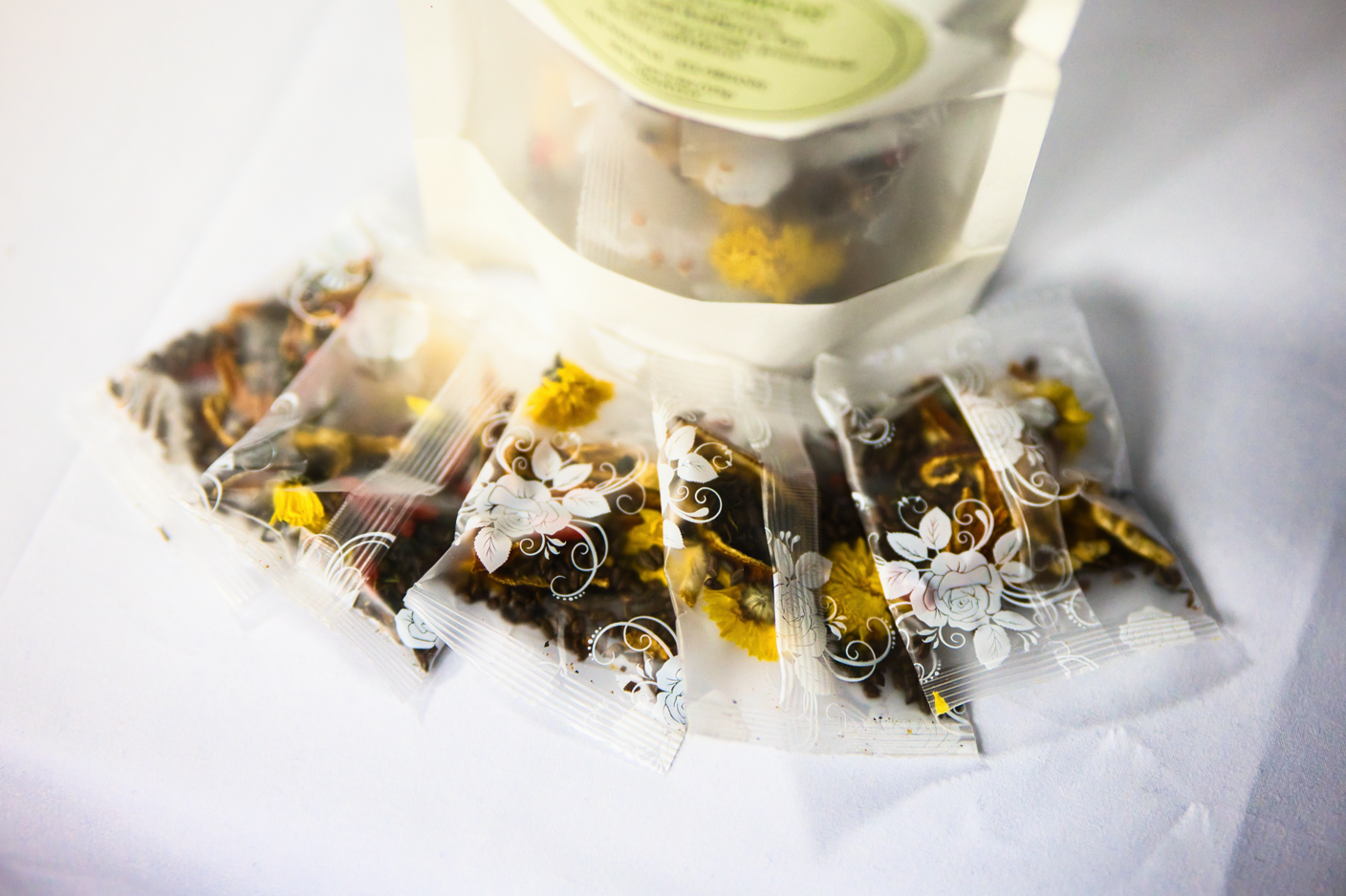 Assorted herbal tea bags in clear plastic packaging with floral decorations and yellow dried flowers, placed on a white surface.
