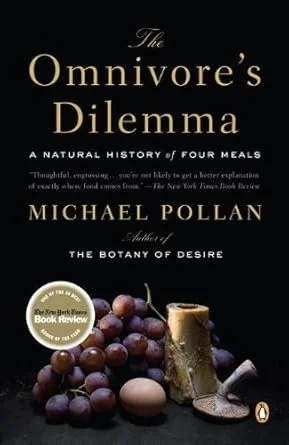 The cover of a book titled 'The Omnivore's Dilemma' by Michael Pollan, featuring grapes, a mushroom, an egg, and a glass of wine or juice on a dark background.