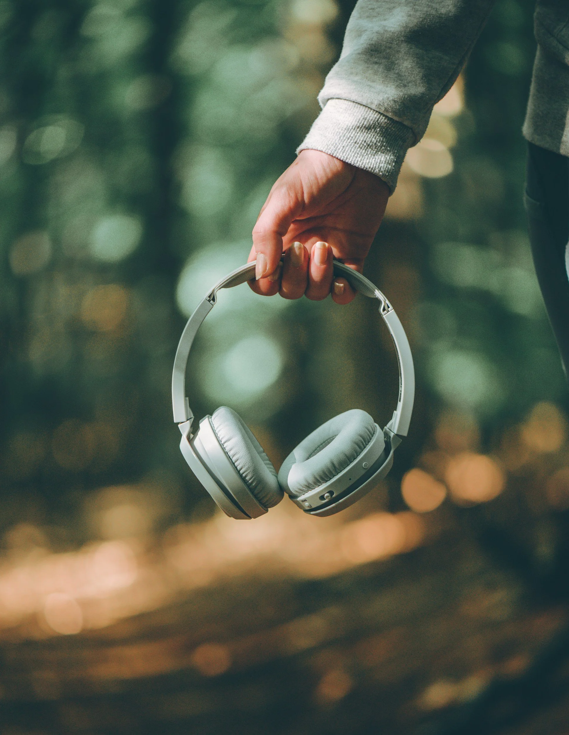 Woman holding headphones in a natural settings surrounding by greenery, representing the relief and calmness from EMDR therapy.