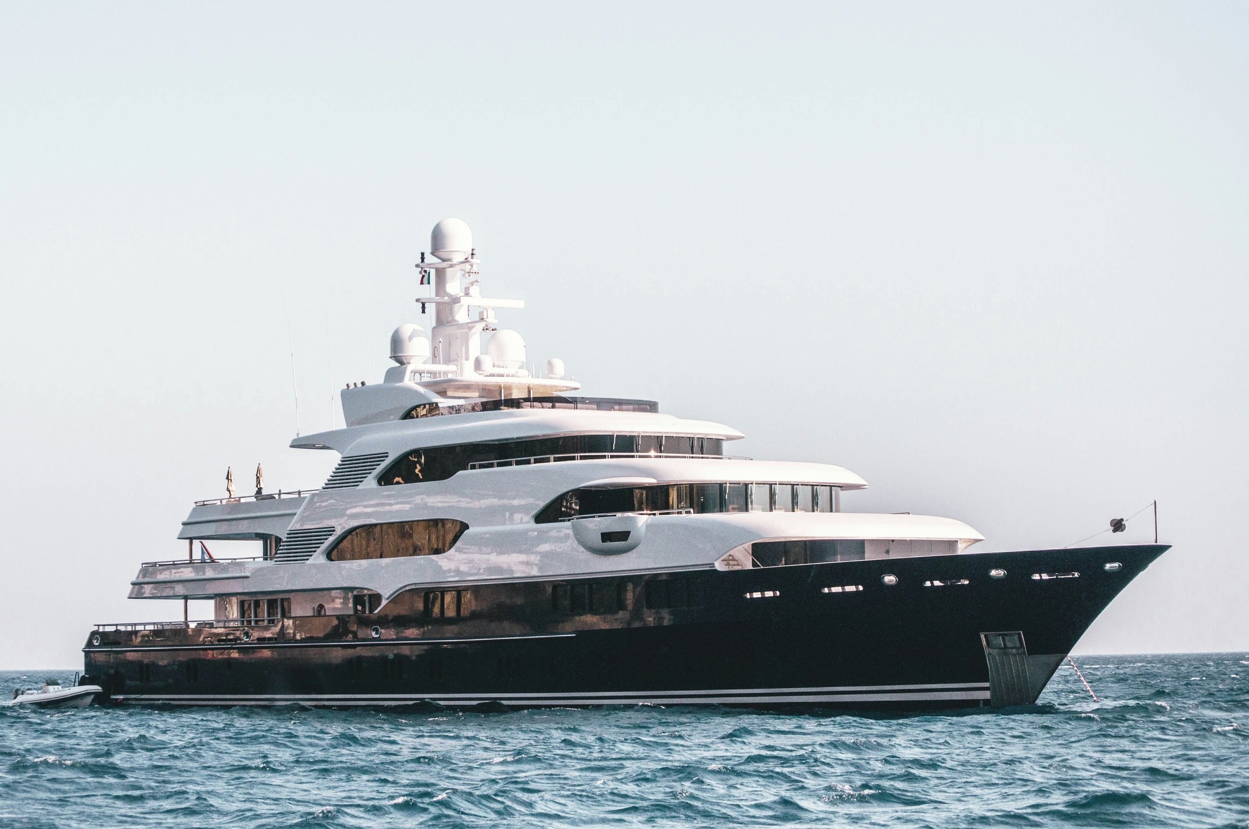 Un grand yacht blanc naviguant sur la mer calme avec un ciel dégagé en arrière-plan.
