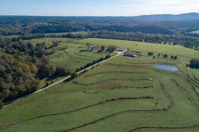 Ariel view of farm with green swales, pond, and house with mountains in the background