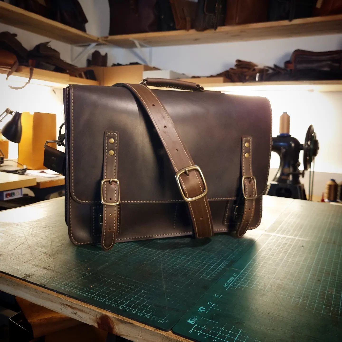 Maletín de cuero marrón con correas ajustables, colocado sobre una mesa de trabajo en un taller de artesanía.