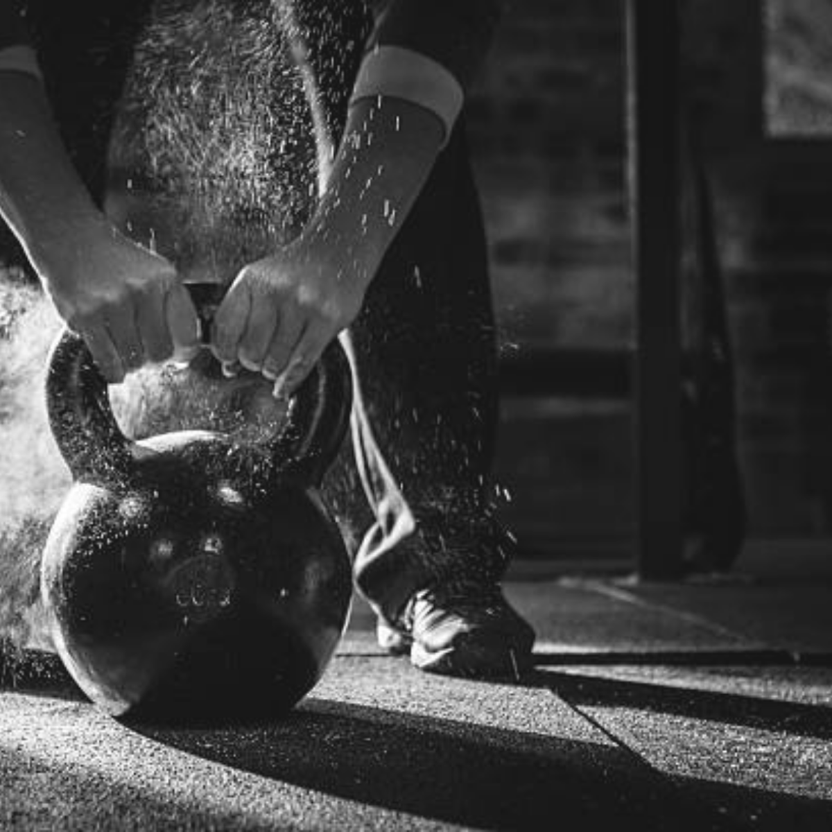 Person lifting a kettlebell during a workout, with chalk dust in the air, in a gym setting.