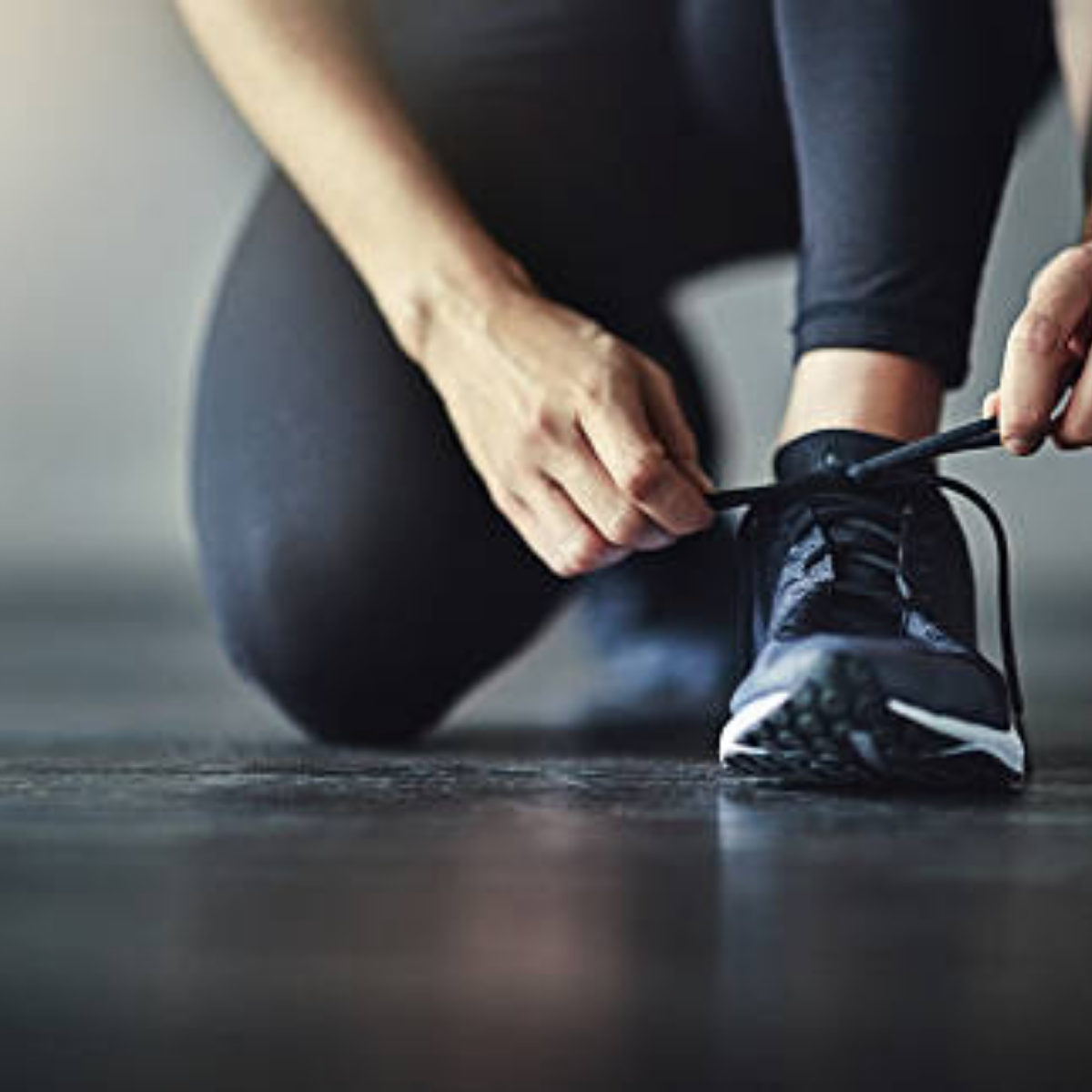 Person tying shoelaces on a black athletic shoe while kneeling on the ground