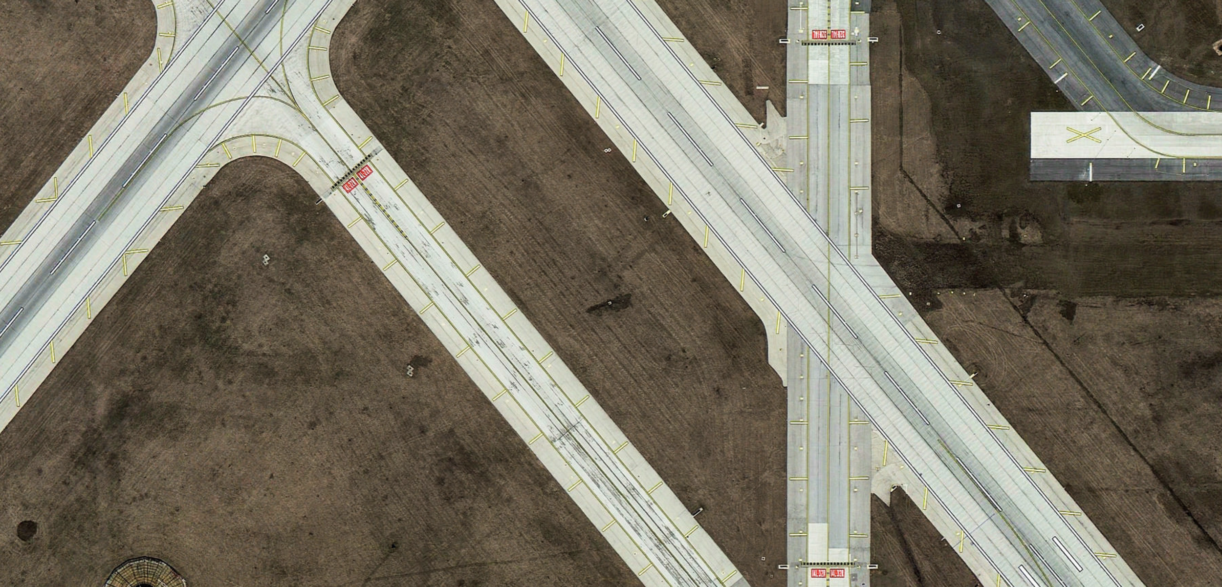 An aerial view of a highway interchange with multiple roads, overpasses, and ramps, with brown fields surrounding the infrastructure.