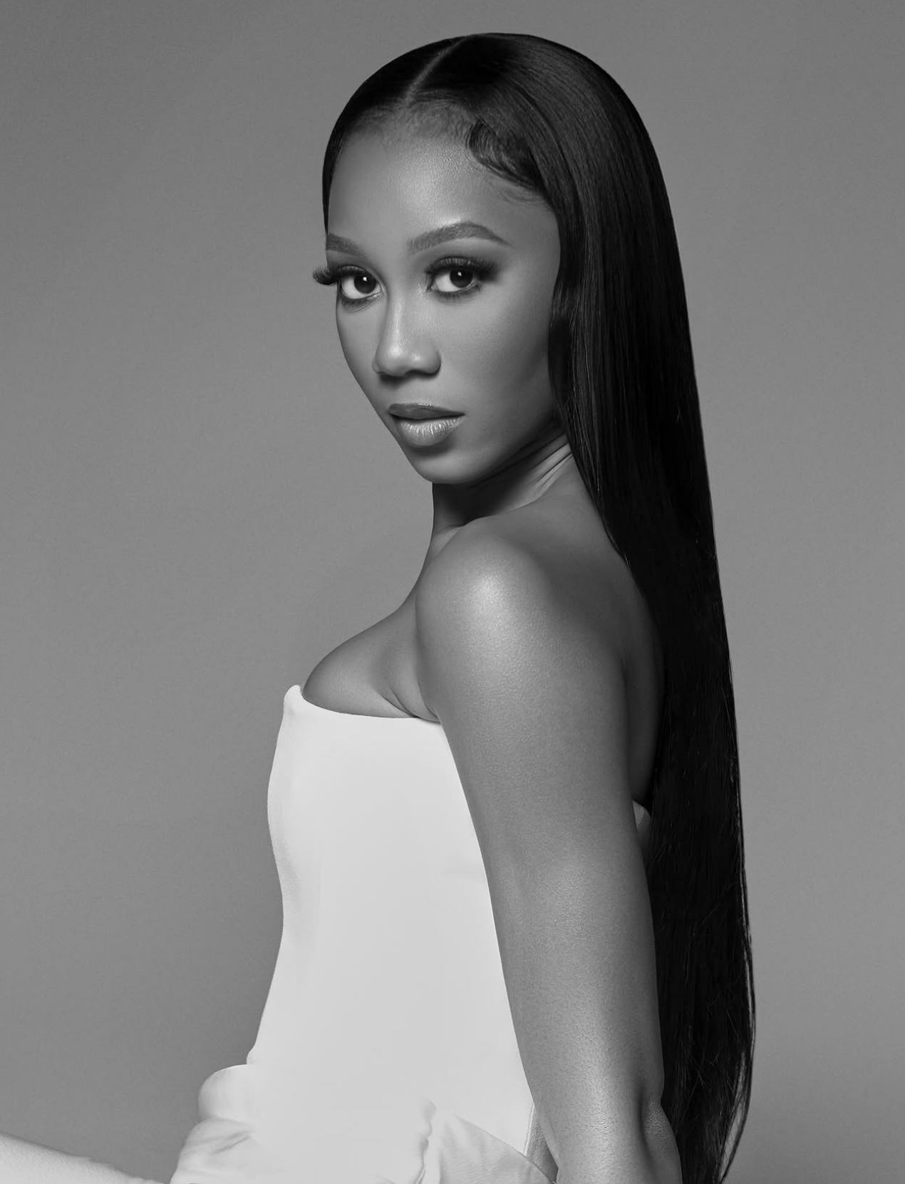 Black and white portrait of a woman with long, straight hair, wearing a strapless dress, looking at the camera.