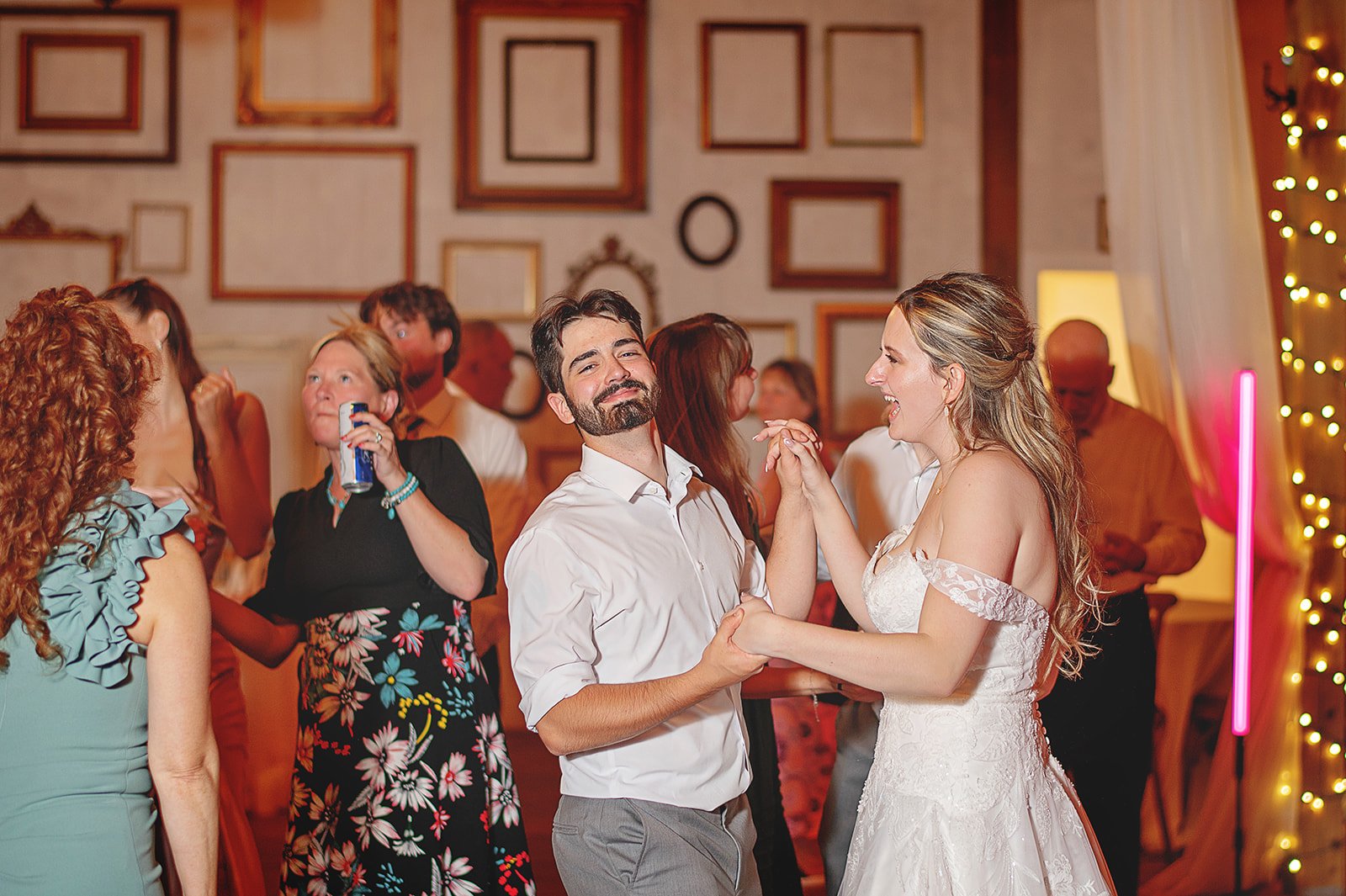 A wedding reception with a bride and groom dancing happily, surrounded by guests in a decorated indoor venue.