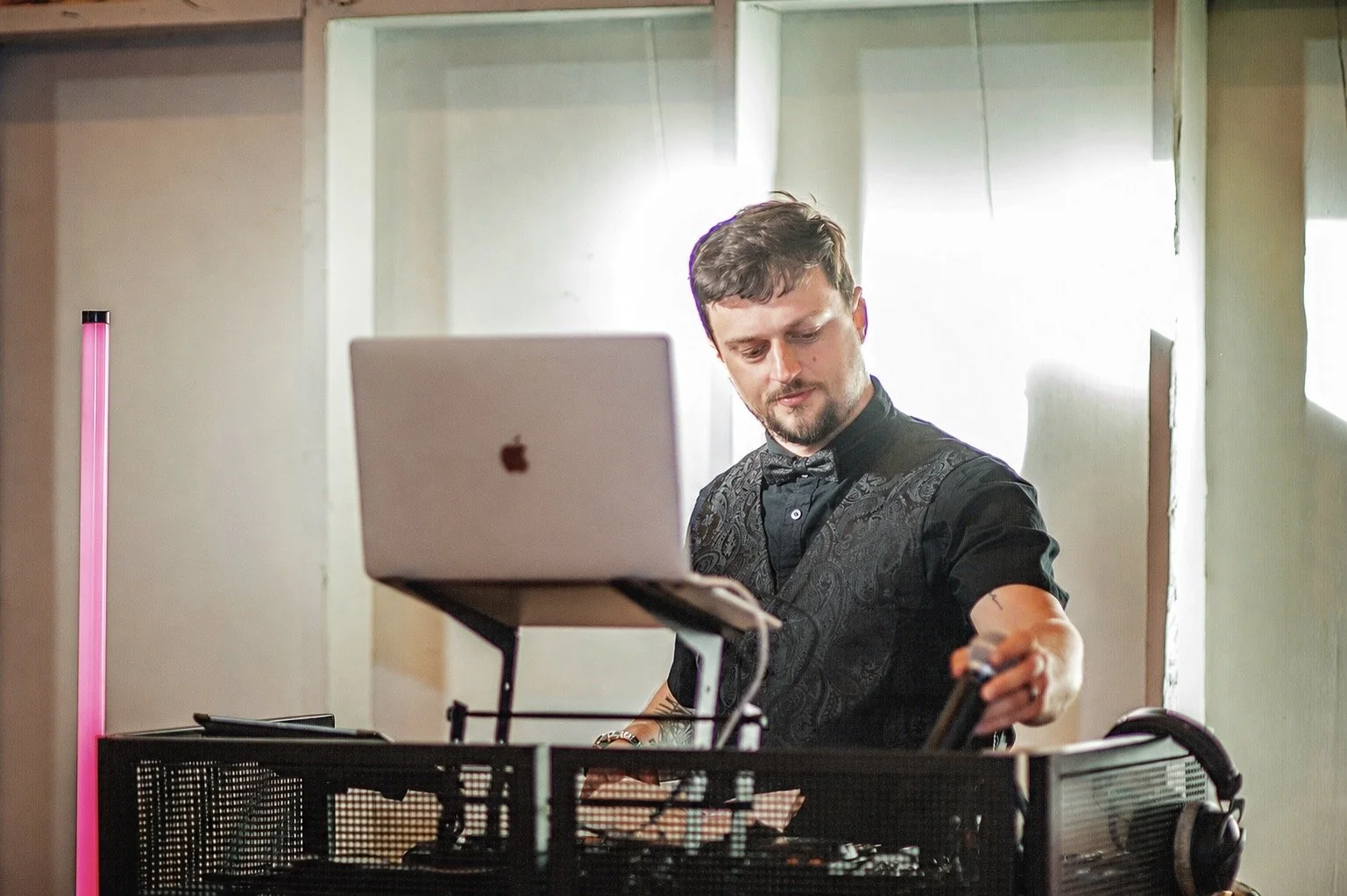 A man DJing holding a microphone in front of a DJ Booth with a Computer,